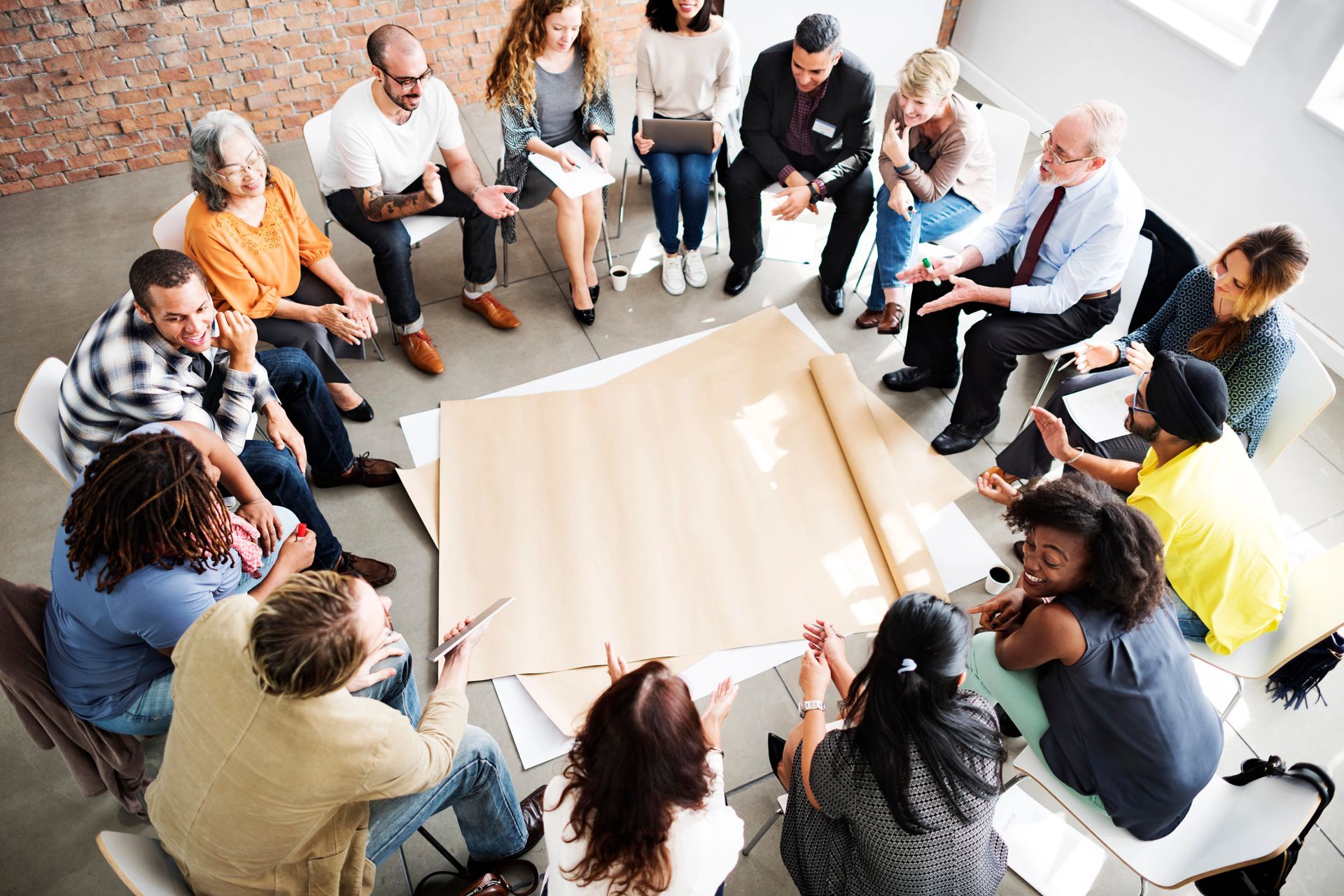 People seated in a circle around a table, engaged in a group discussion in a bright room