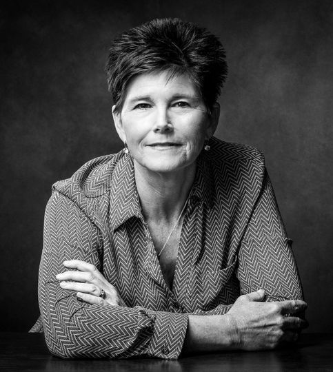 Black-and-white portrait of a Kathy Taylor with short hair, seated with arms crossed and a slight smile