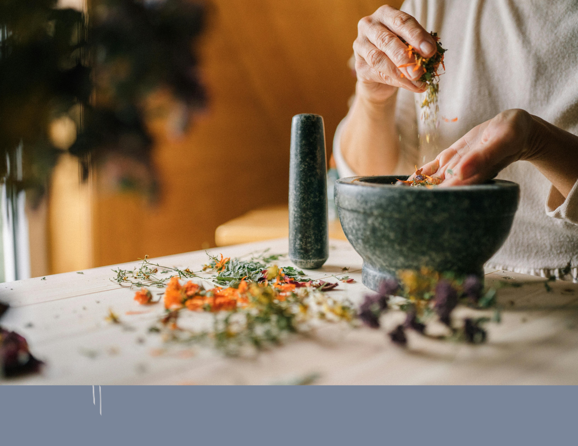 Person grinding herbs in a mortar and pestle on a wooden table.