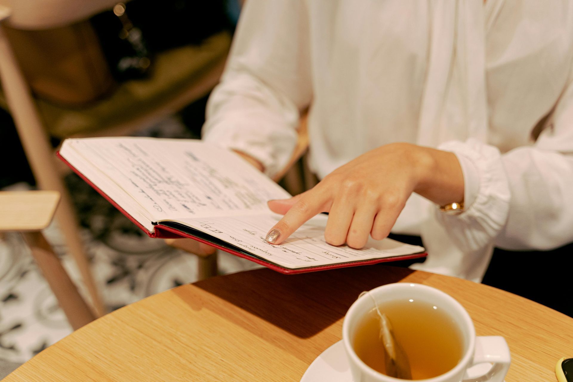 Woman reading a book, finger pointing to text, tea cup on table.