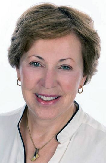 A woman wearing a necklace and earrings is smiling for the camera.