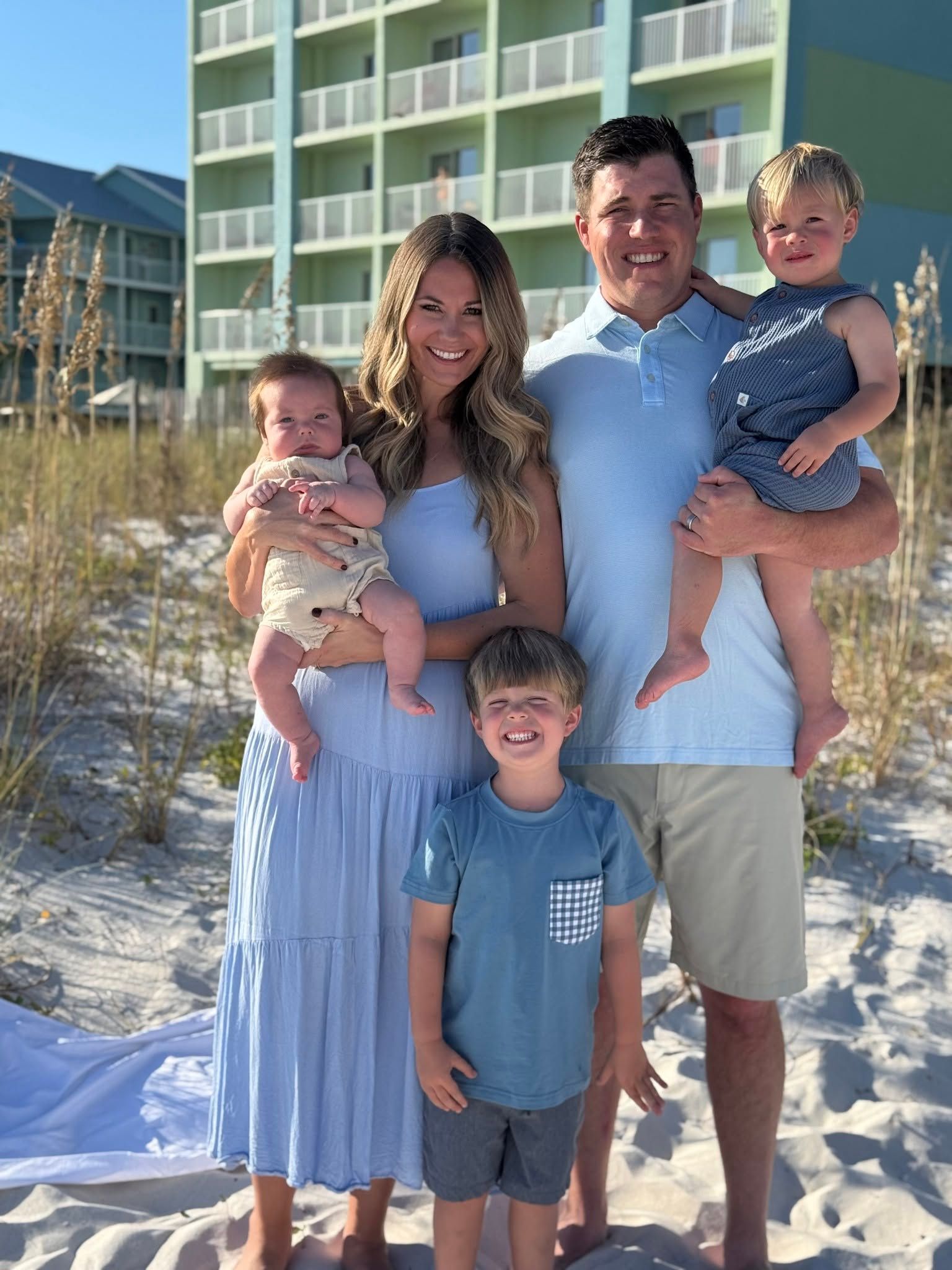 Family of five standing on a snowy beach in front of a resort building, smiling in the sun | KB Motor Works