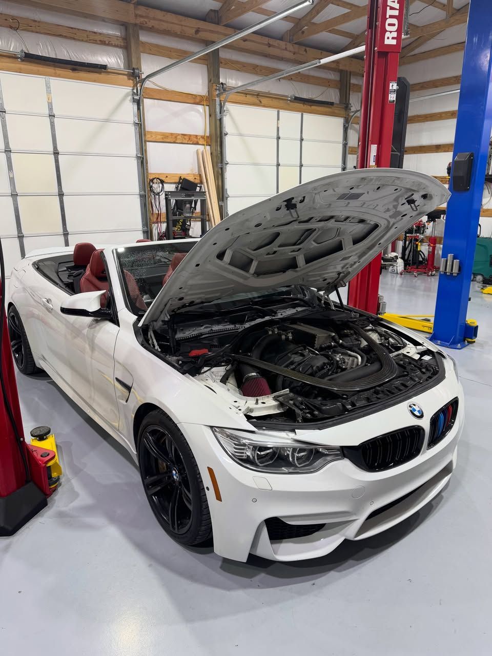 White BMW with hood open in an auto garage, showing engine bay and front bumper missing a headlight | KB Motor Works