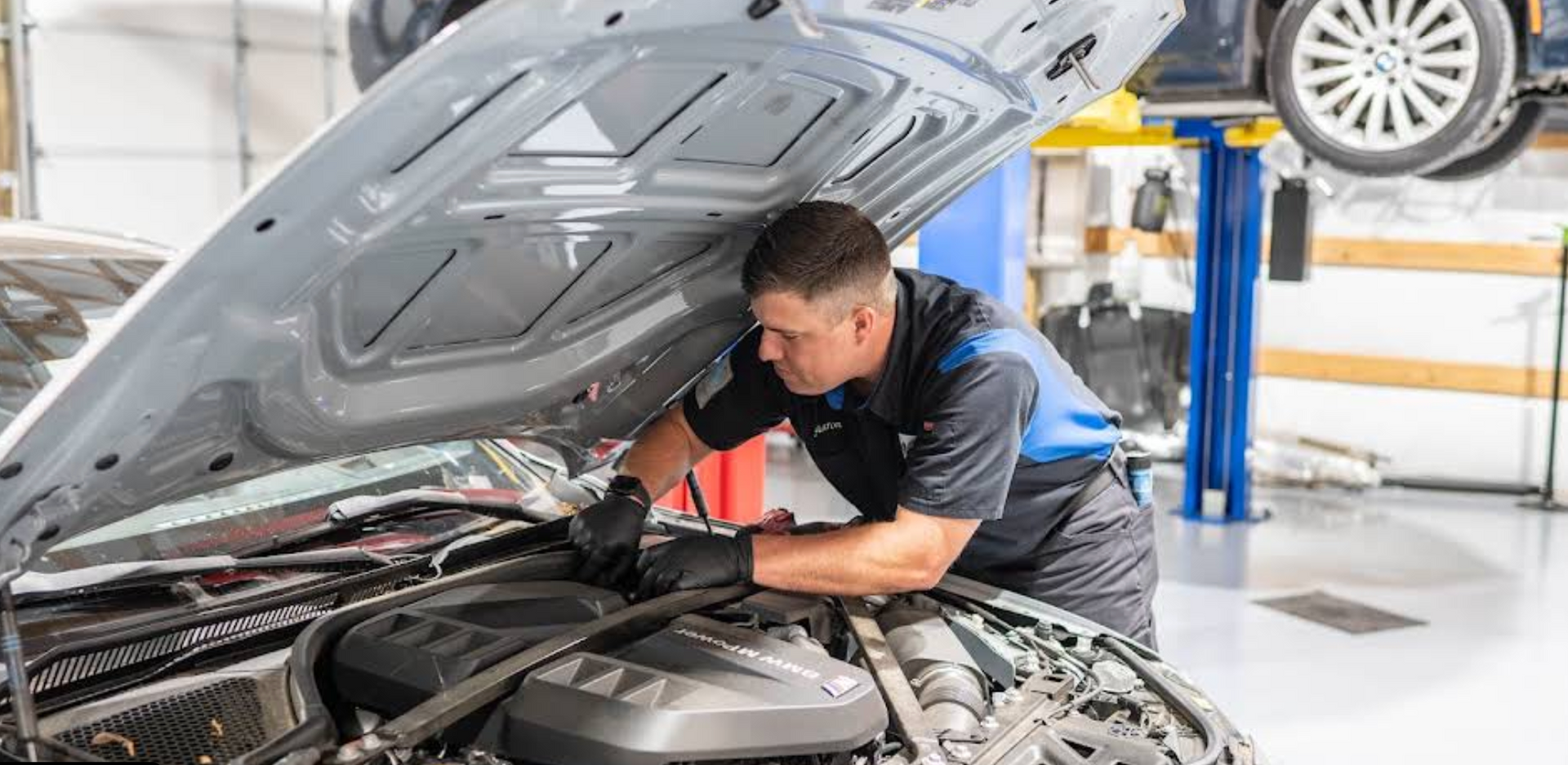 Mechanic inspecting engine under open hood in auto repair shop with car lifted on a hoist | KB Motor Works