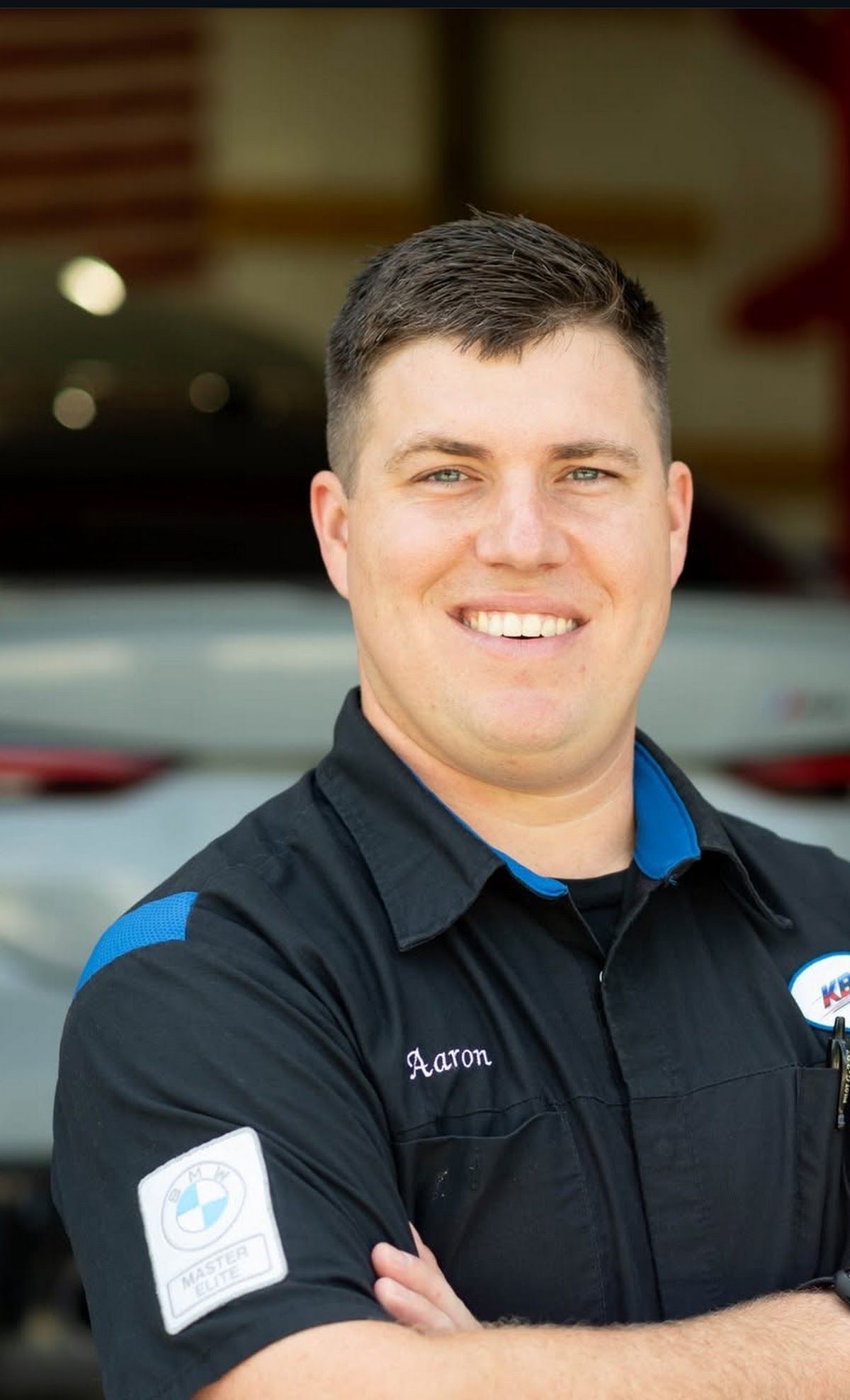 Smiling mechanic in dark work shirt with arms crossed in a garage | KB Motor Works