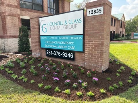 A brick sign for Councill & Glass Dental Group at address 12835, surrounded by a freshly mulched garden with small plants.