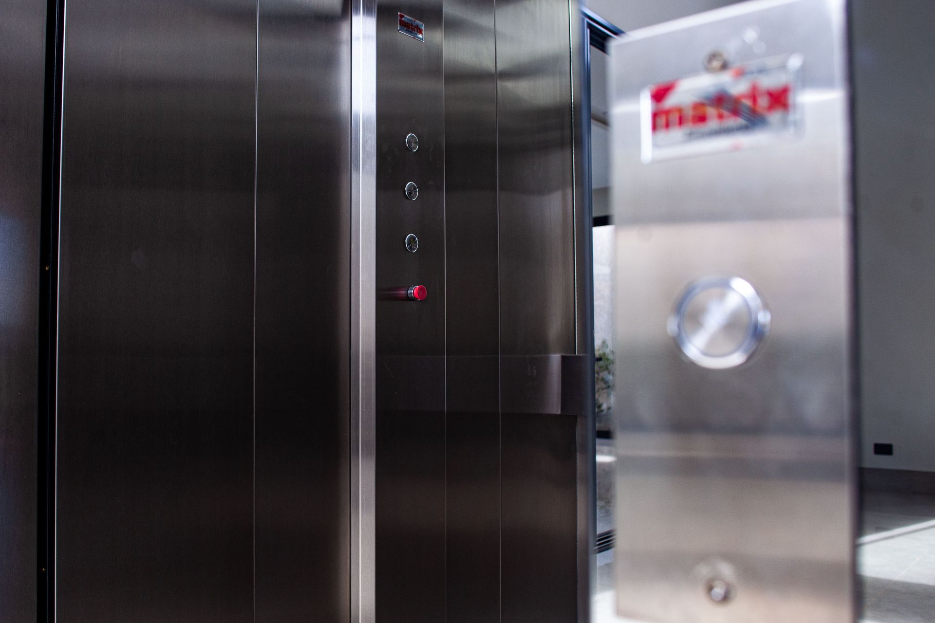 Porta de elevador em aço inoxidável com painel de botões de chamada da marca Matrix à direita.