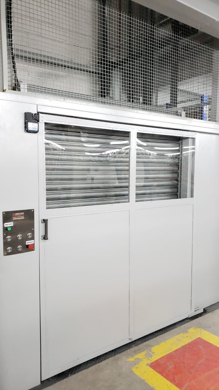 Portas de correr industriais brancas com painéis de ripas horizontais e um painel de controle adjacente, instaladas no local.