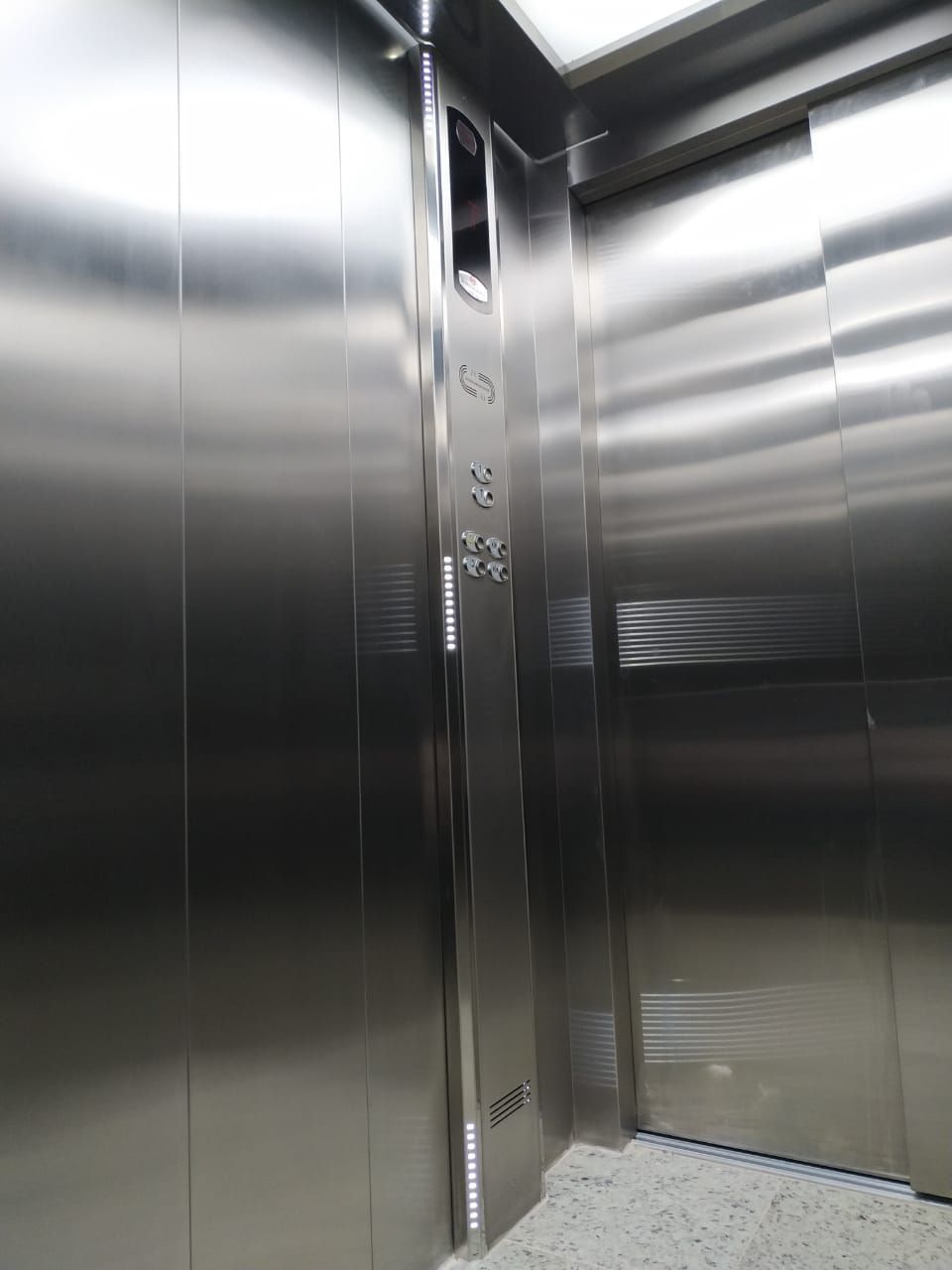 Interior de um elevador moderno em aço inoxidável com painel de controle e paredes refletoras.