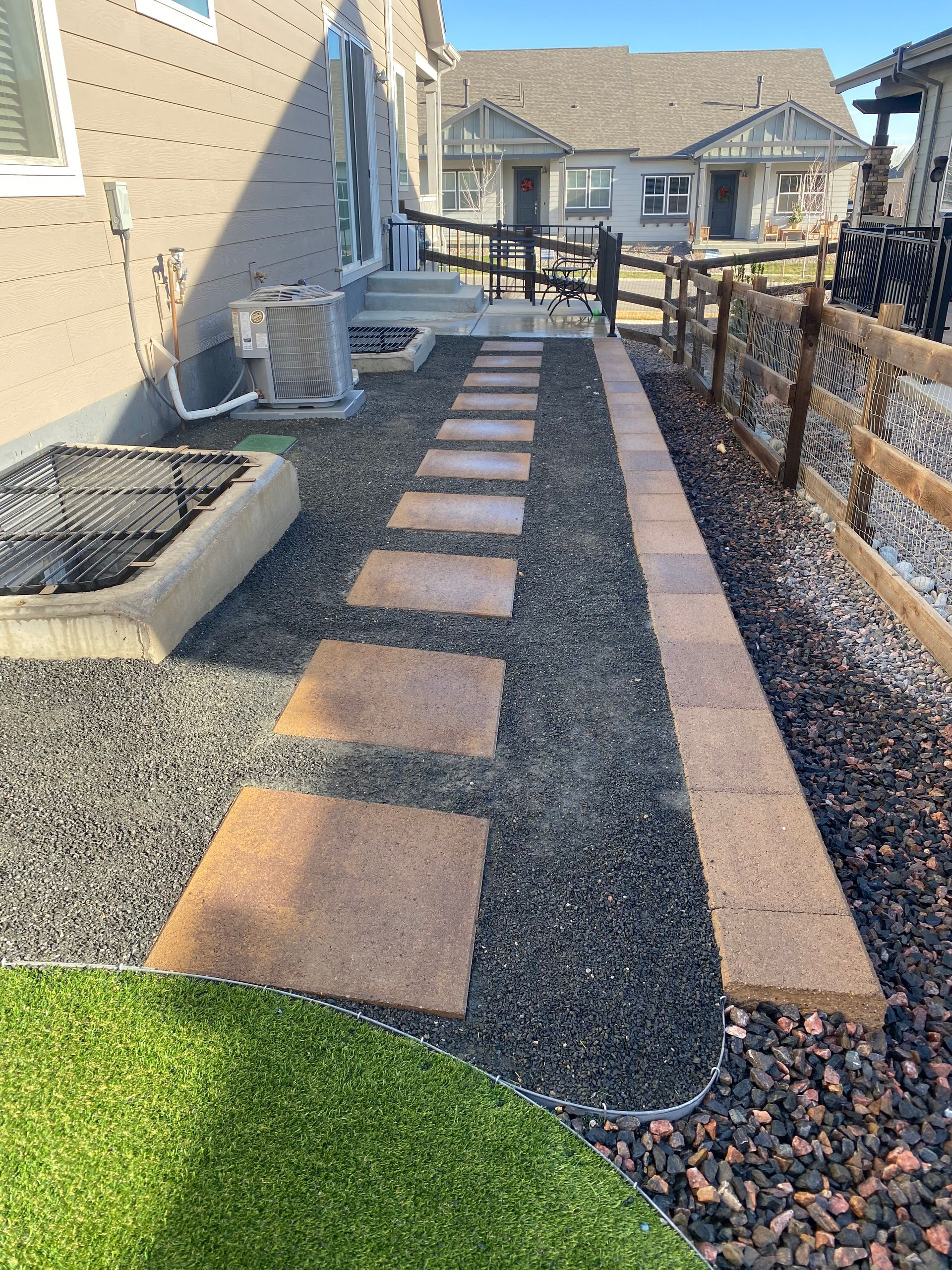 Gravel path with stepping stones beside a beige house and black fence in a landscaped yard