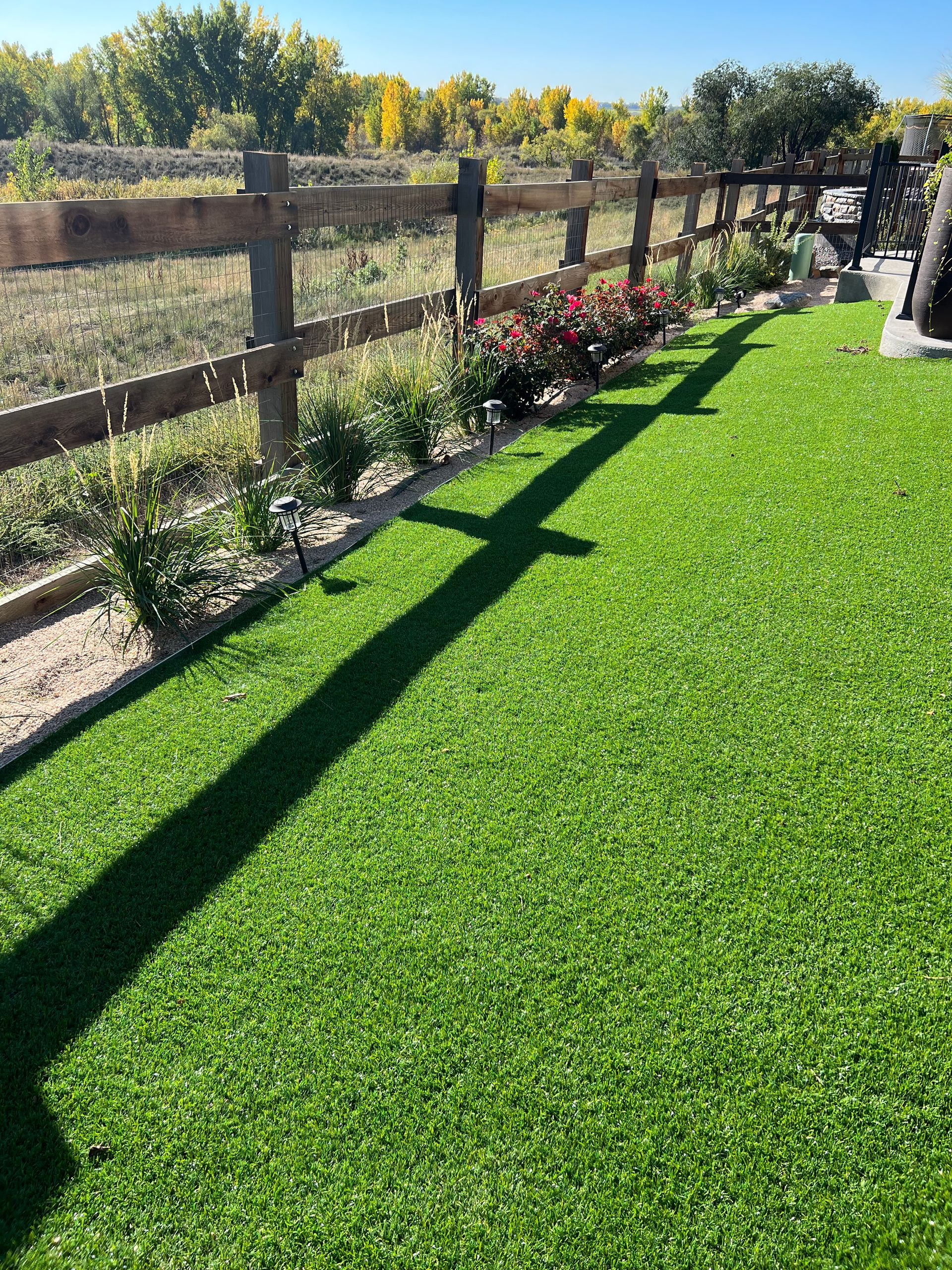 Sunlit backyard with artificial grass, wooden fence, and small flower beds along the edge