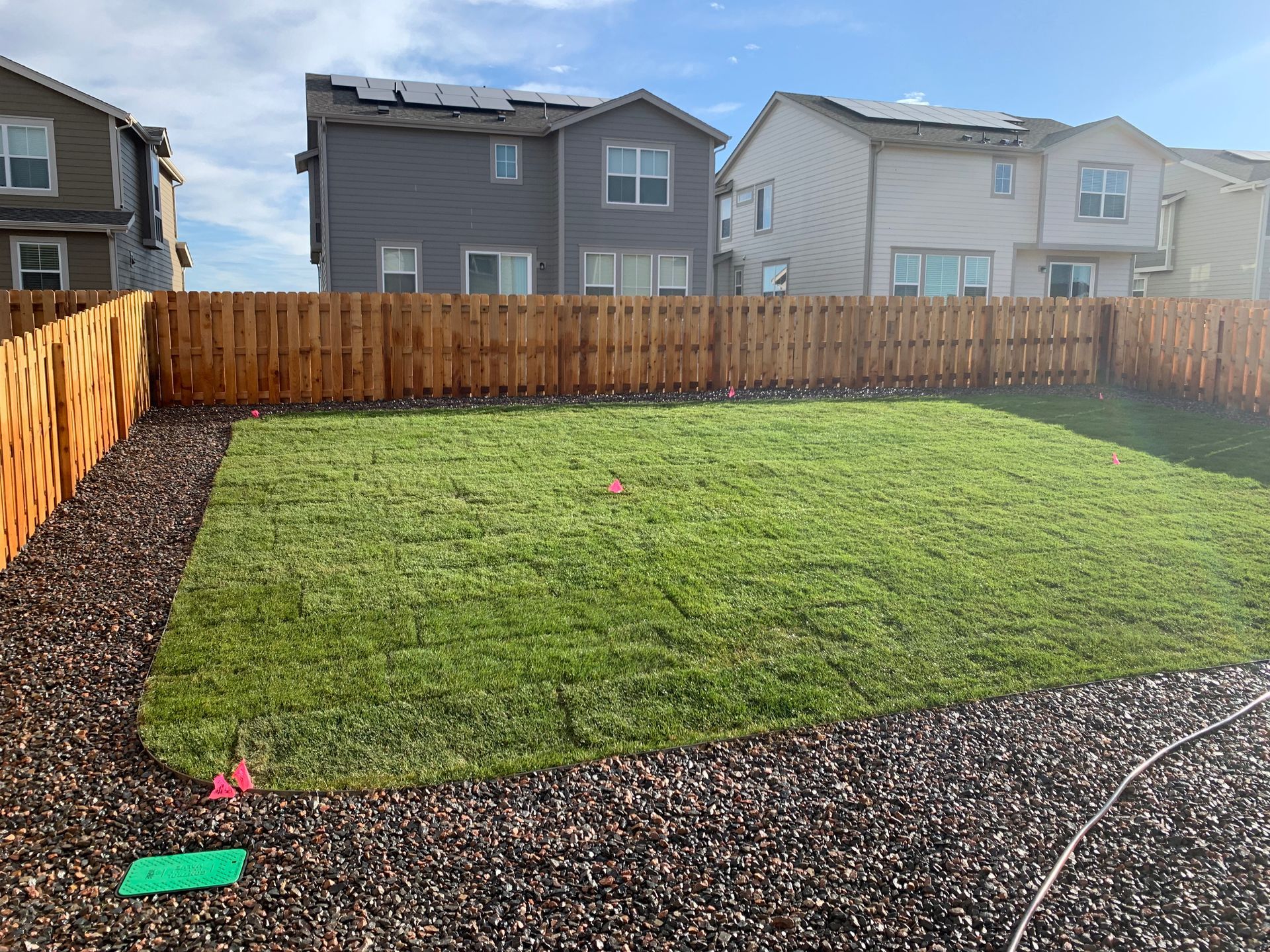 Backyard with a green lawn, wooden fence, and gravel border in a suburban neighborhood