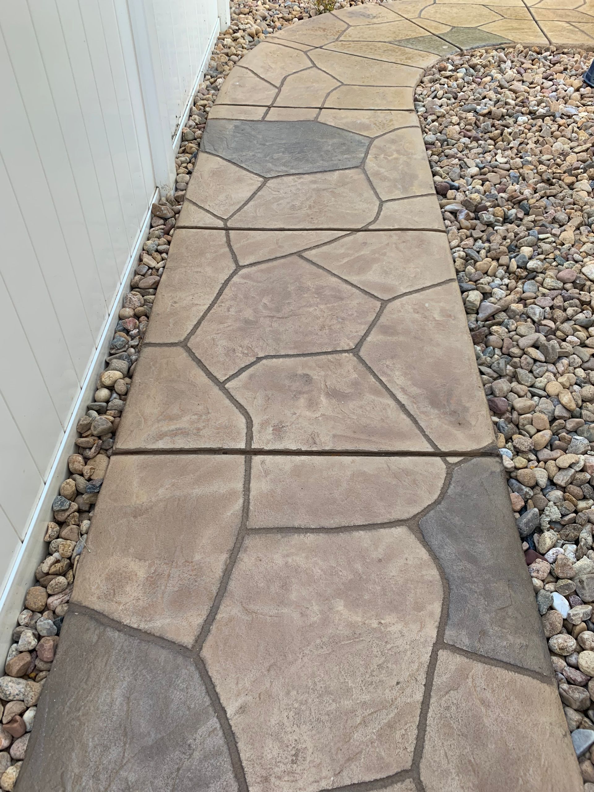 Stone walkway beside a white fence and gravel border in a backyard