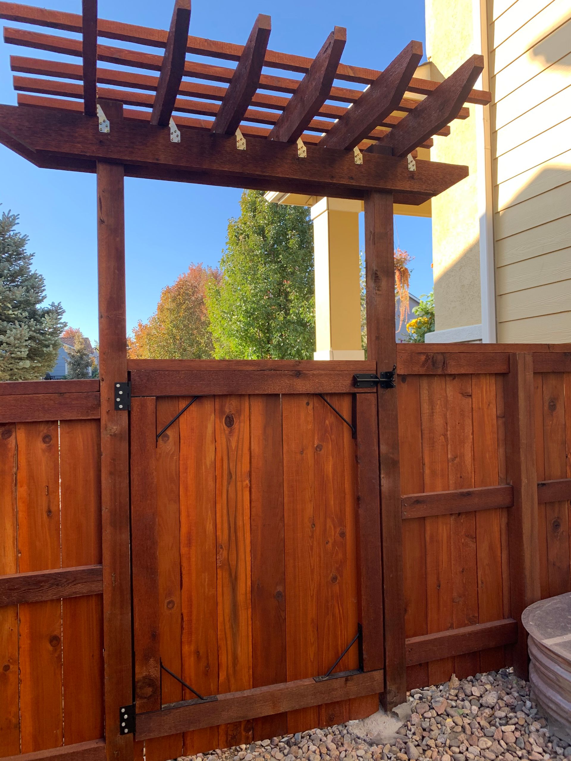 Wooden backyard gate and fence with pergola overhead, lit by warm sunlight