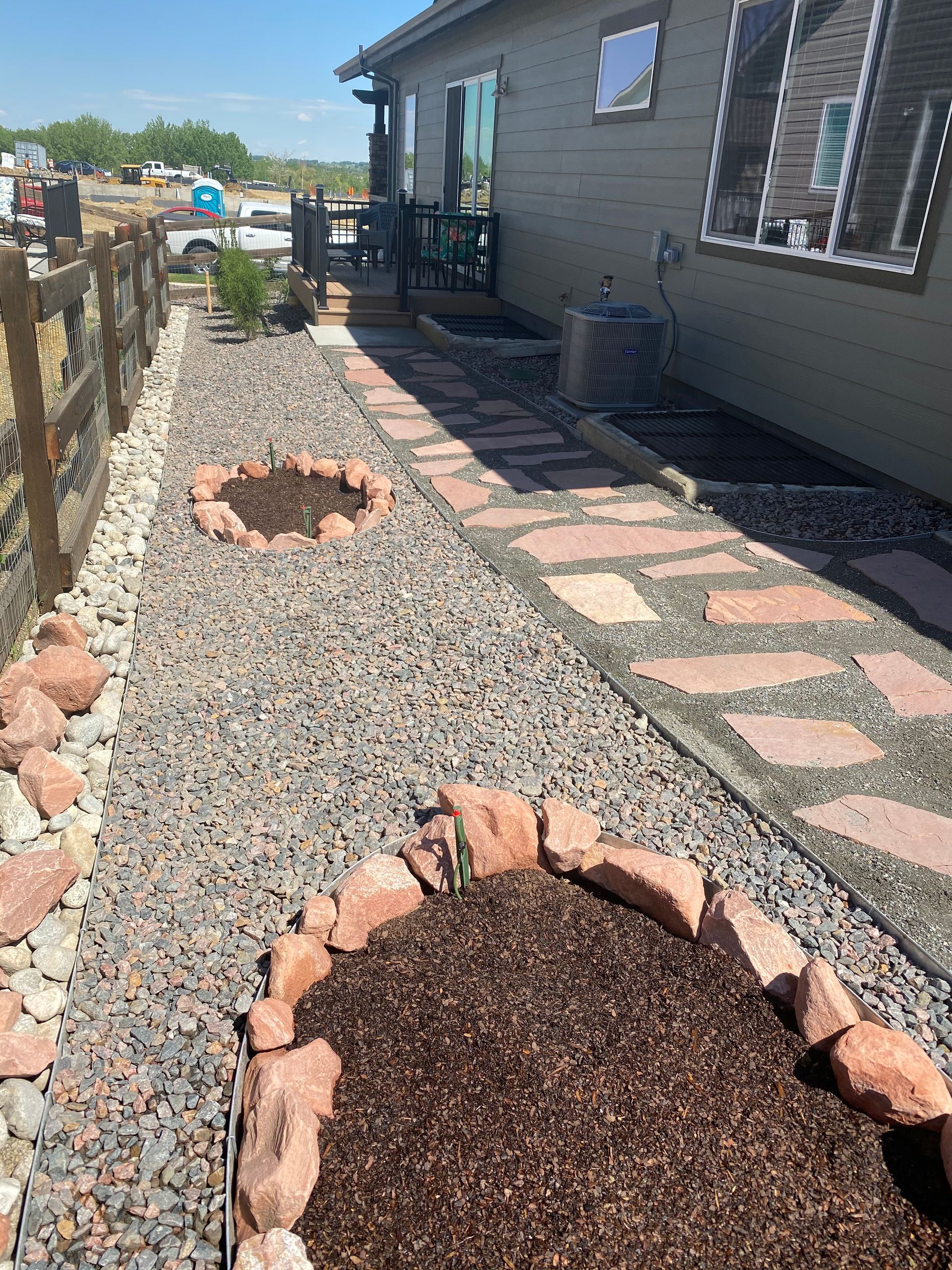Backyard landscaping with gravel, stone pavers, and two circular brick-edged garden beds beside a house