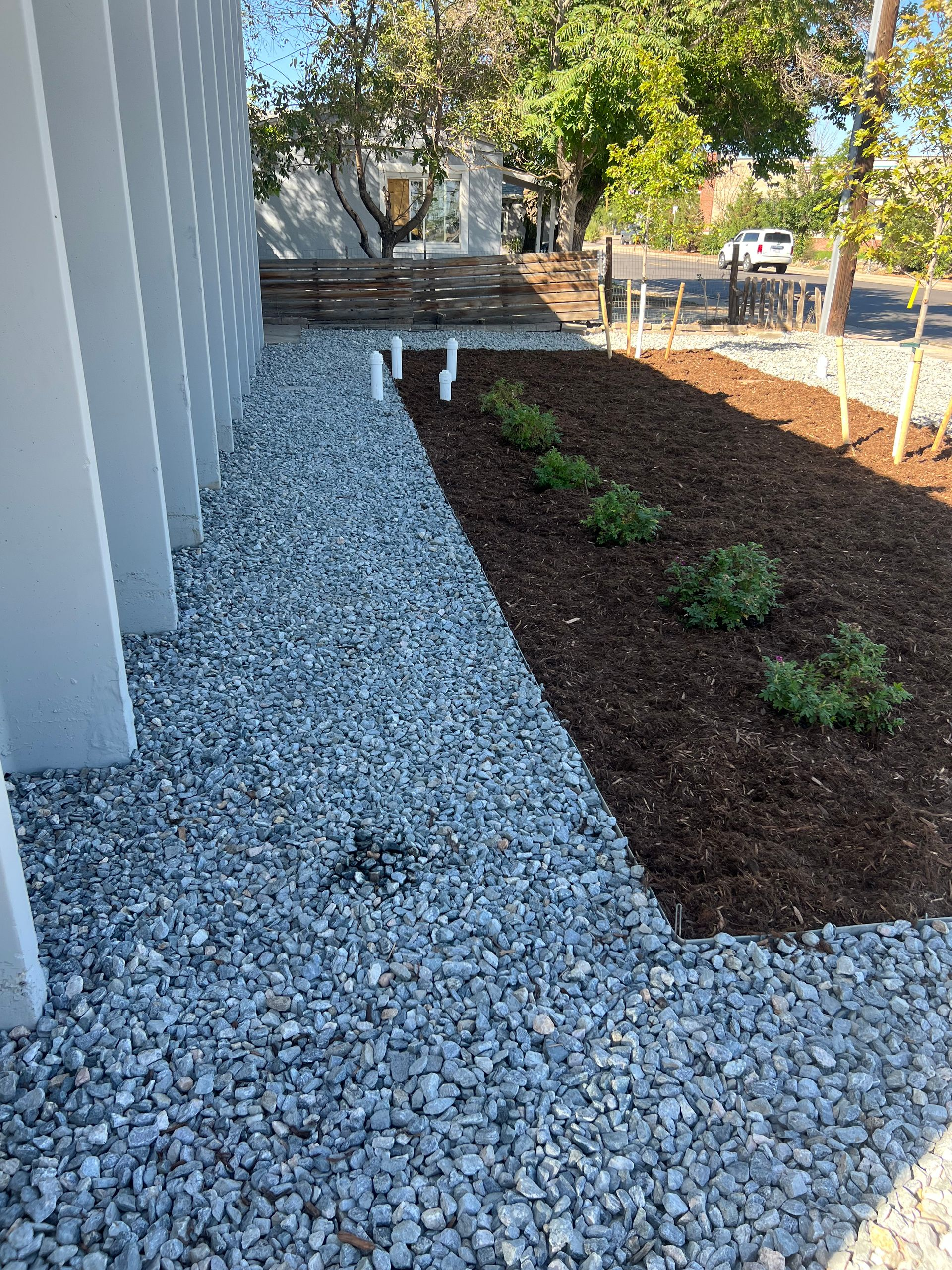 Landscaped walkway with white gravel, dark mulch bed, and small shrubs beside a building.