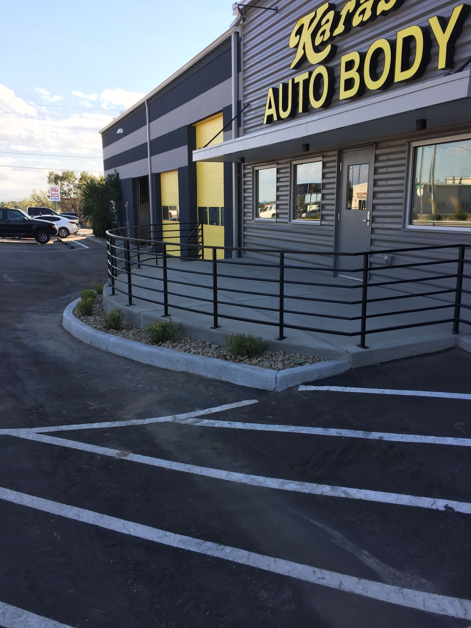 Auto body shop exterior with yellow sign, gray building, and empty parking lot at dusk