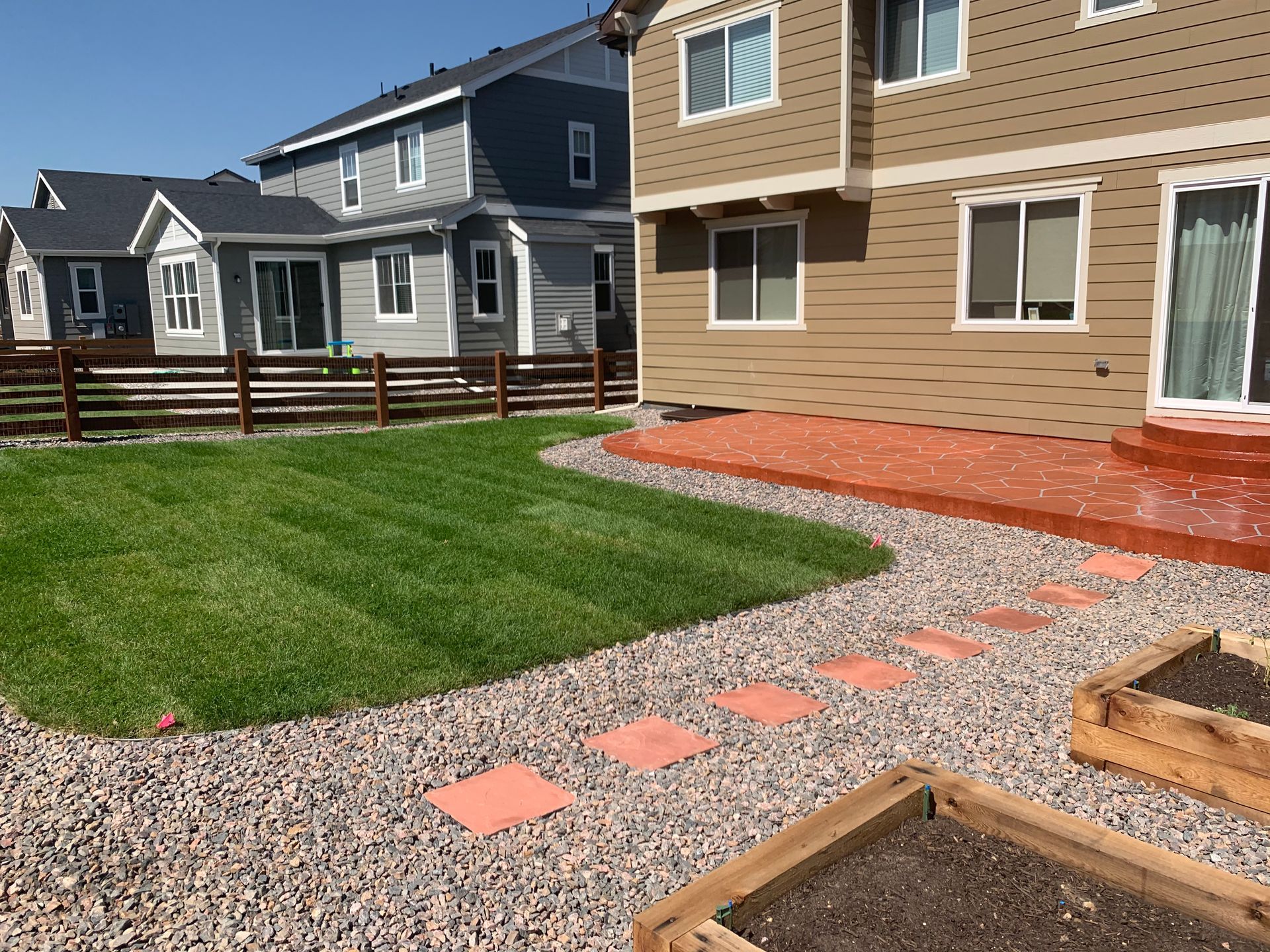 Backyard patio with gravel path, green lawn, wooden deck, and row of suburban houses