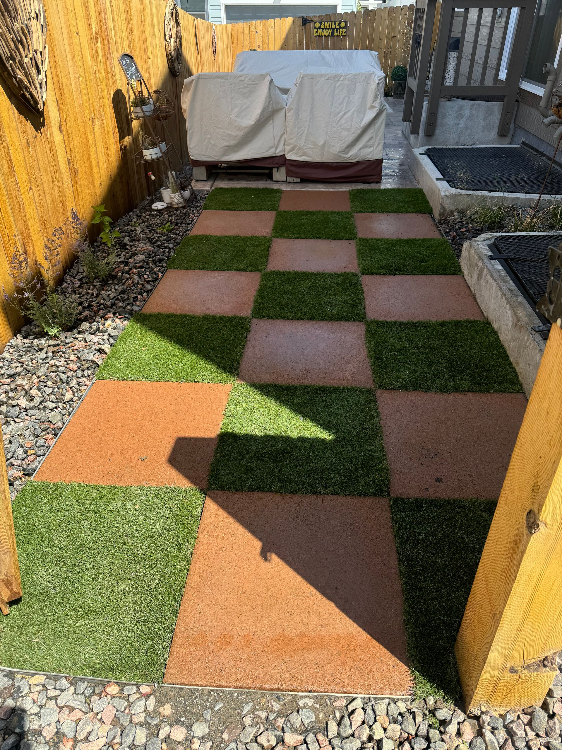 Checkered garden path with orange and green pavers, flanked by gravel beds and wooden fences