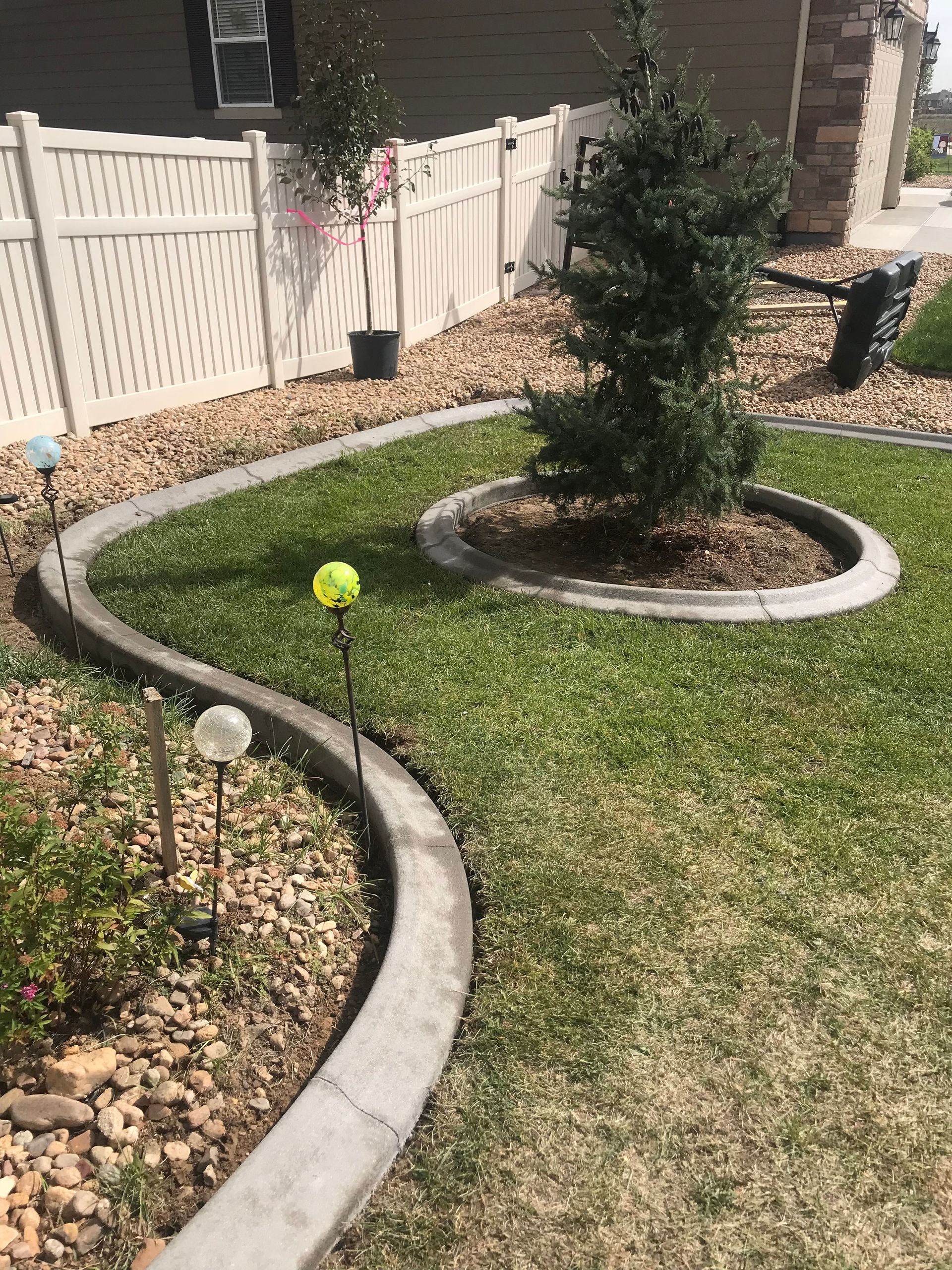Curved stone edging borders a landscaped yard with mulch, grass, and a small evergreen tree.