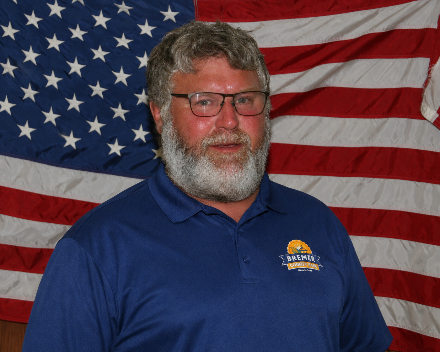 Man standing indoors in front of a U.S. flag, wearing a green Carhartt sweatshirt.