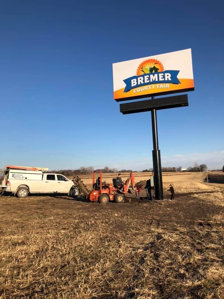 Roadside Bremer sign on a tall pole beside a white pickup and red tractor in a dry field under blue sky