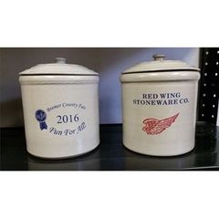 Two white Red Wing Stoneware crocks with lids on a shelf, one labeled 2016 and the other Red Wing Stoneware Co.