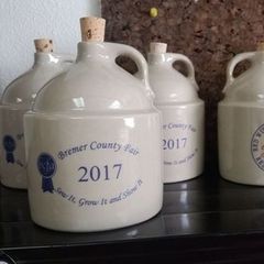 Ceramic cream jugs with cork stoppers on a shelf, labeled “Bremer County Fair 2017.”