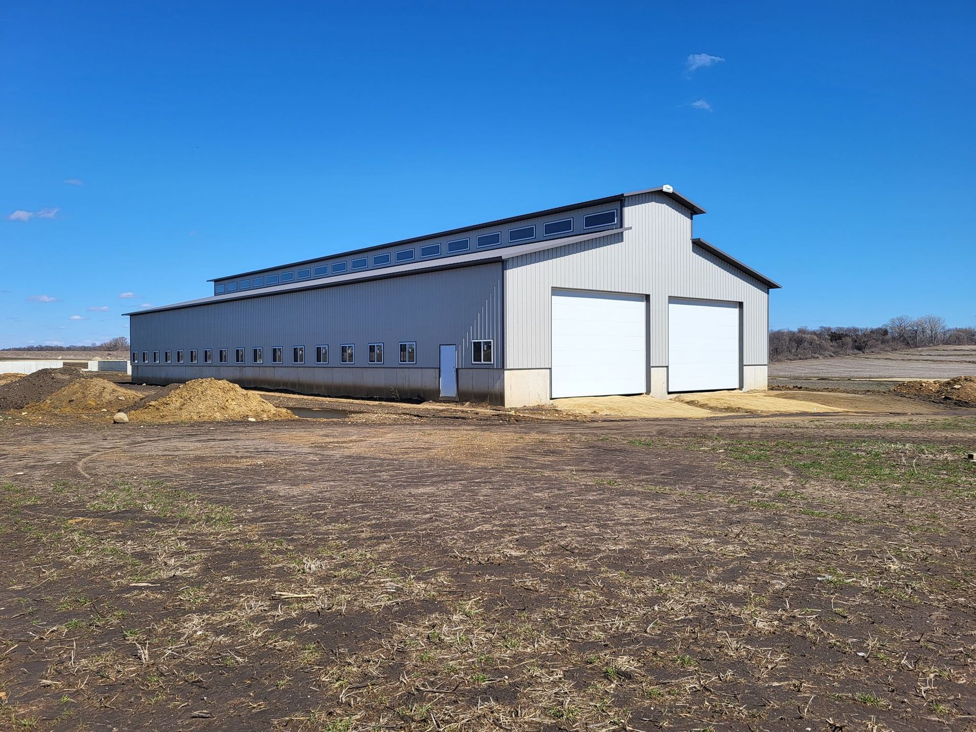 Large gray metal barn with white doors in a grassy field under a blue sky