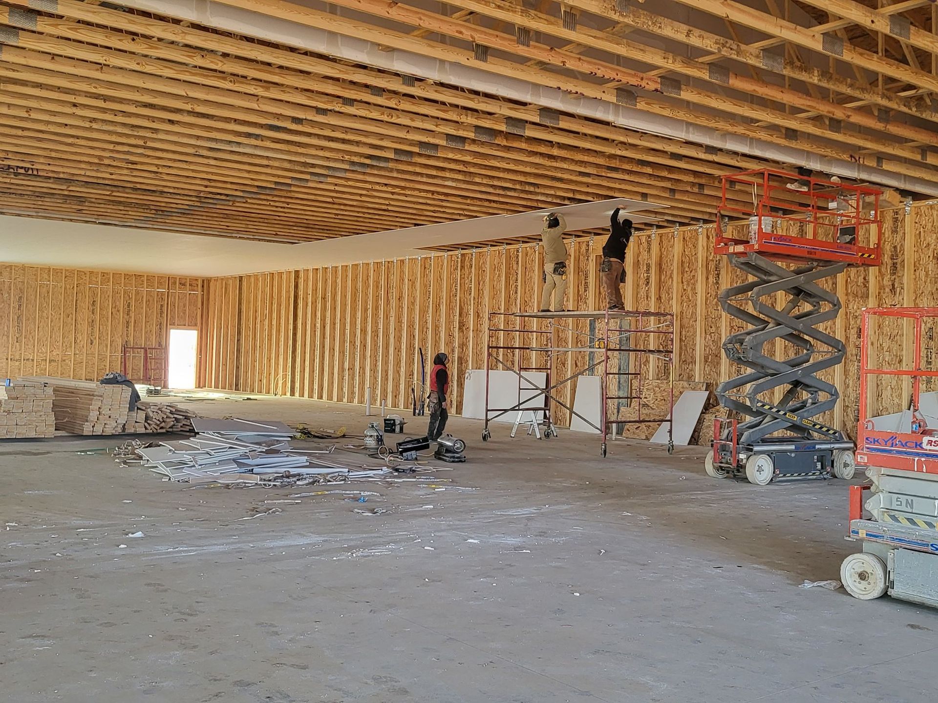 Interior of unfinished wooden building with scissor lift, scaffolding, and construction debris on concrete floor