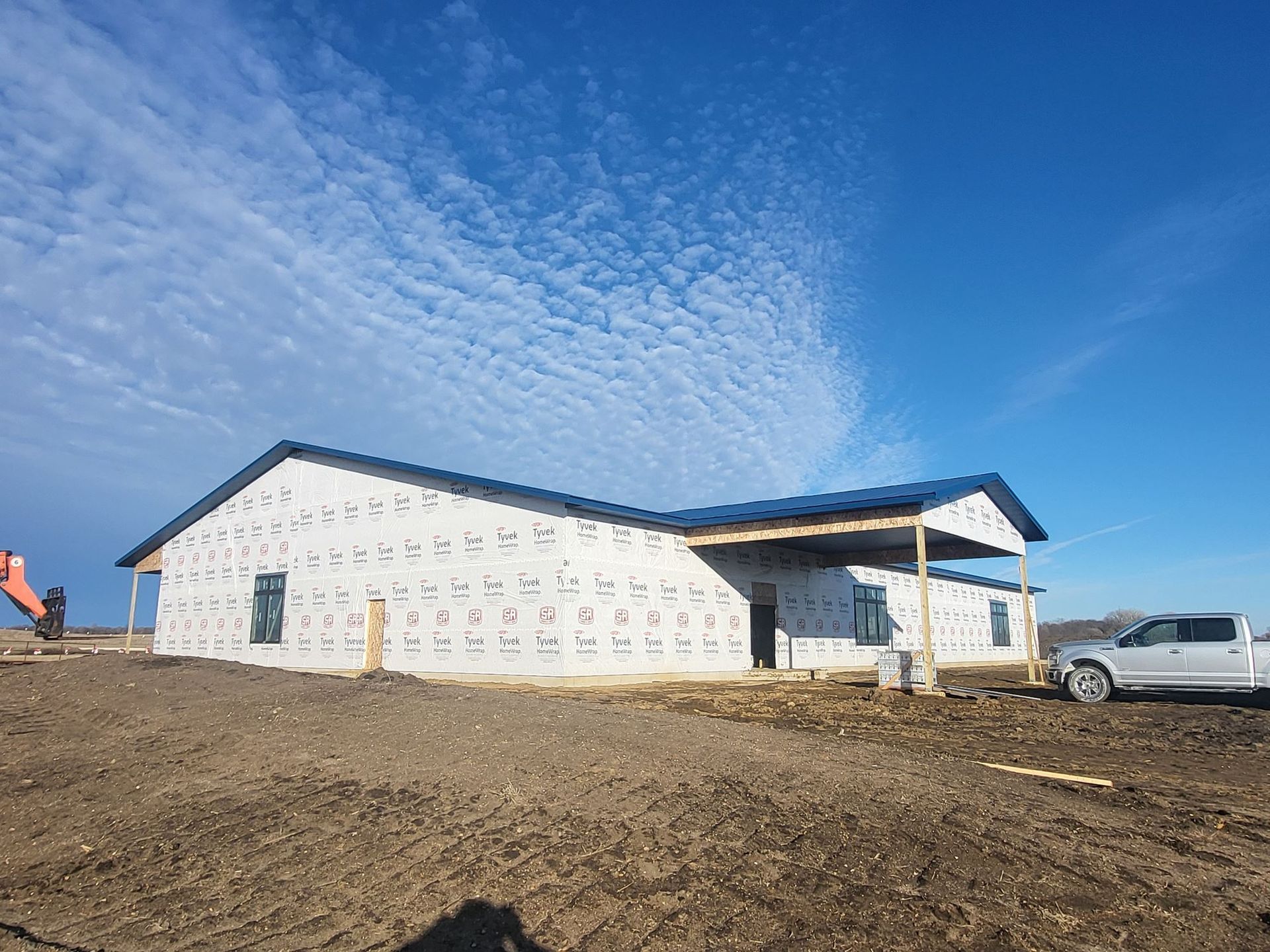 Partially built house wrapped in white sheathing under a blue sky, with a pickup truck nearby