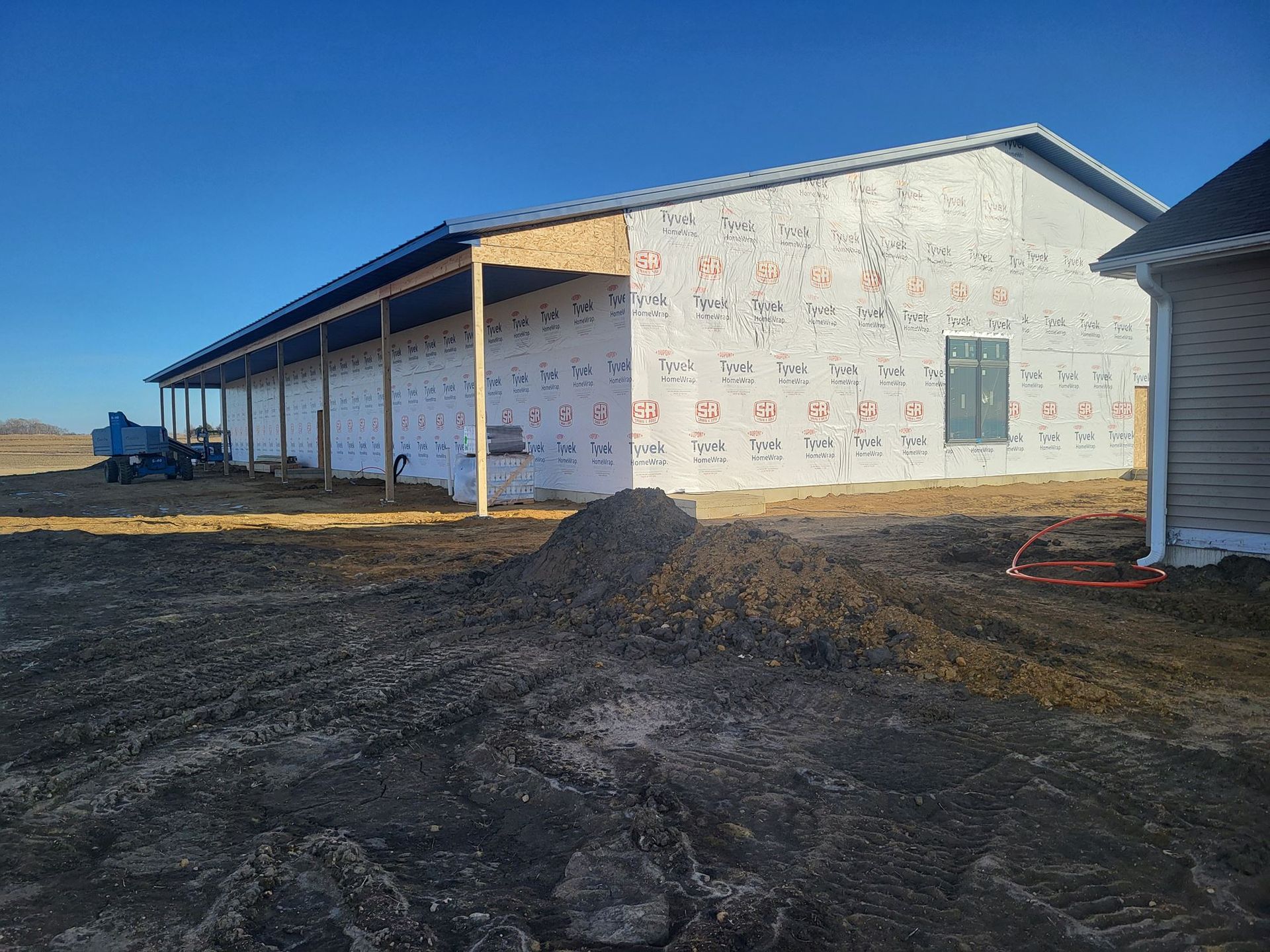 Partially built house with white exterior, covered porch, and dirt lot under a clear sky