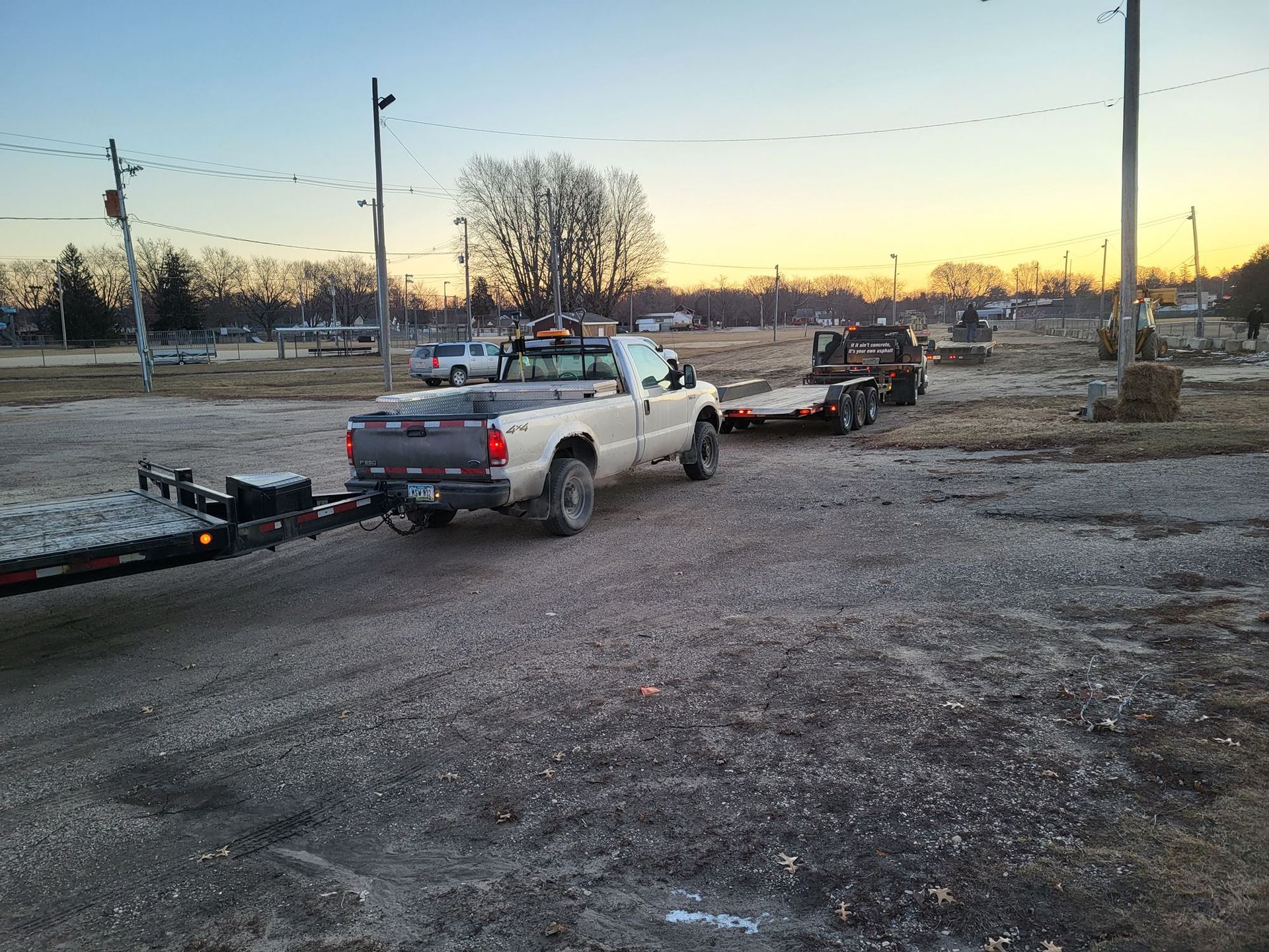Silver pickup truck towing a trailer on a gravel lot at sunset