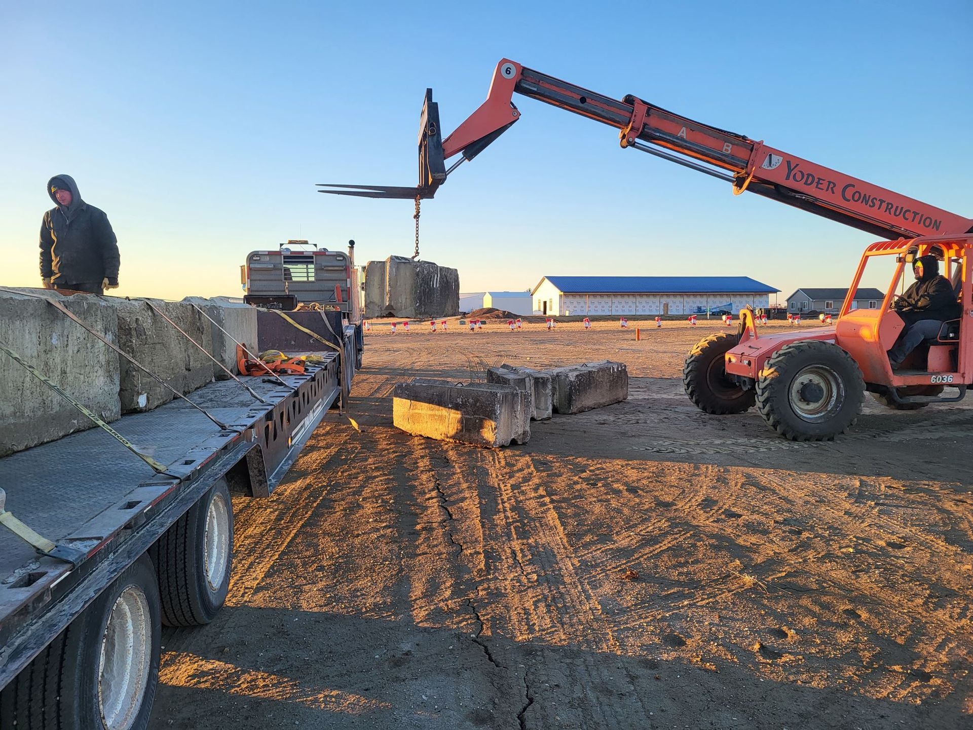 Construction site with a telehandler lifting concrete blocks beside a truck at sunset