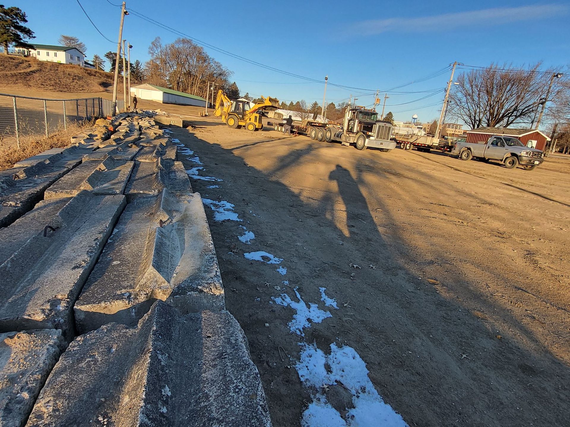 Snow-lined dirt road beside parked vehicles and construction equipment at sunset
