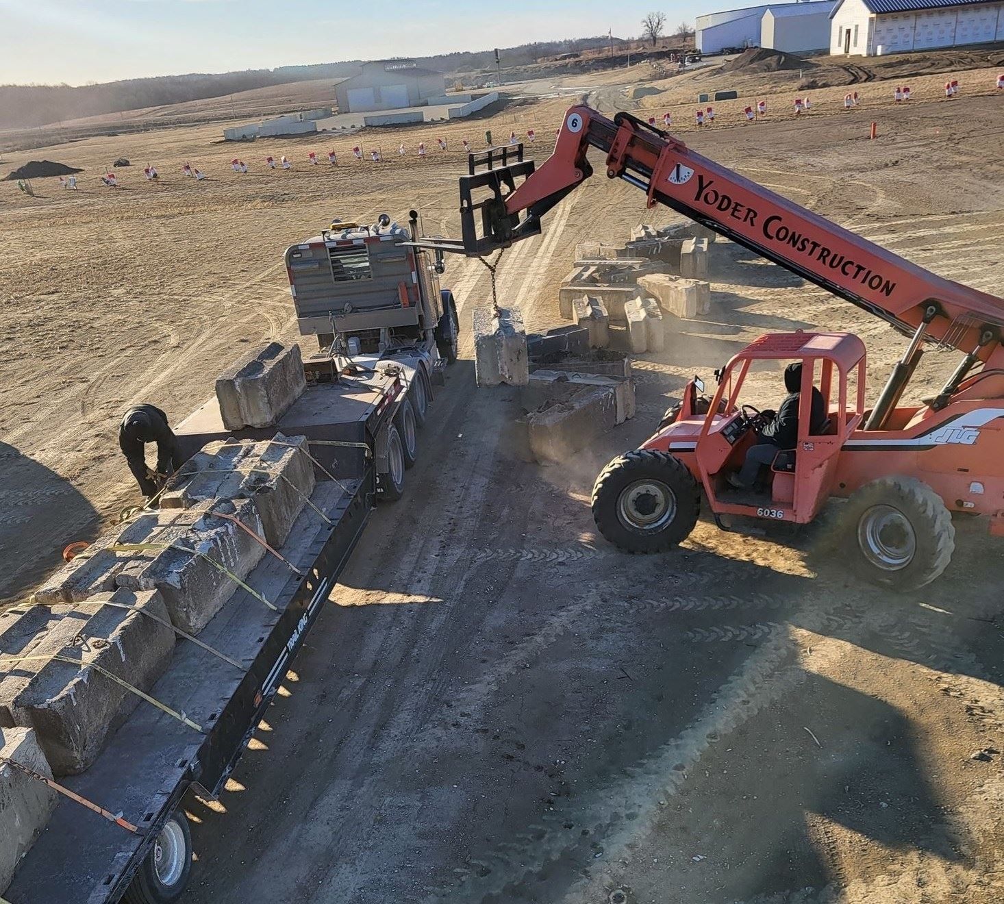Excavator loading broken concrete blocks into a dump truck on a dirt road in a rural worksite.