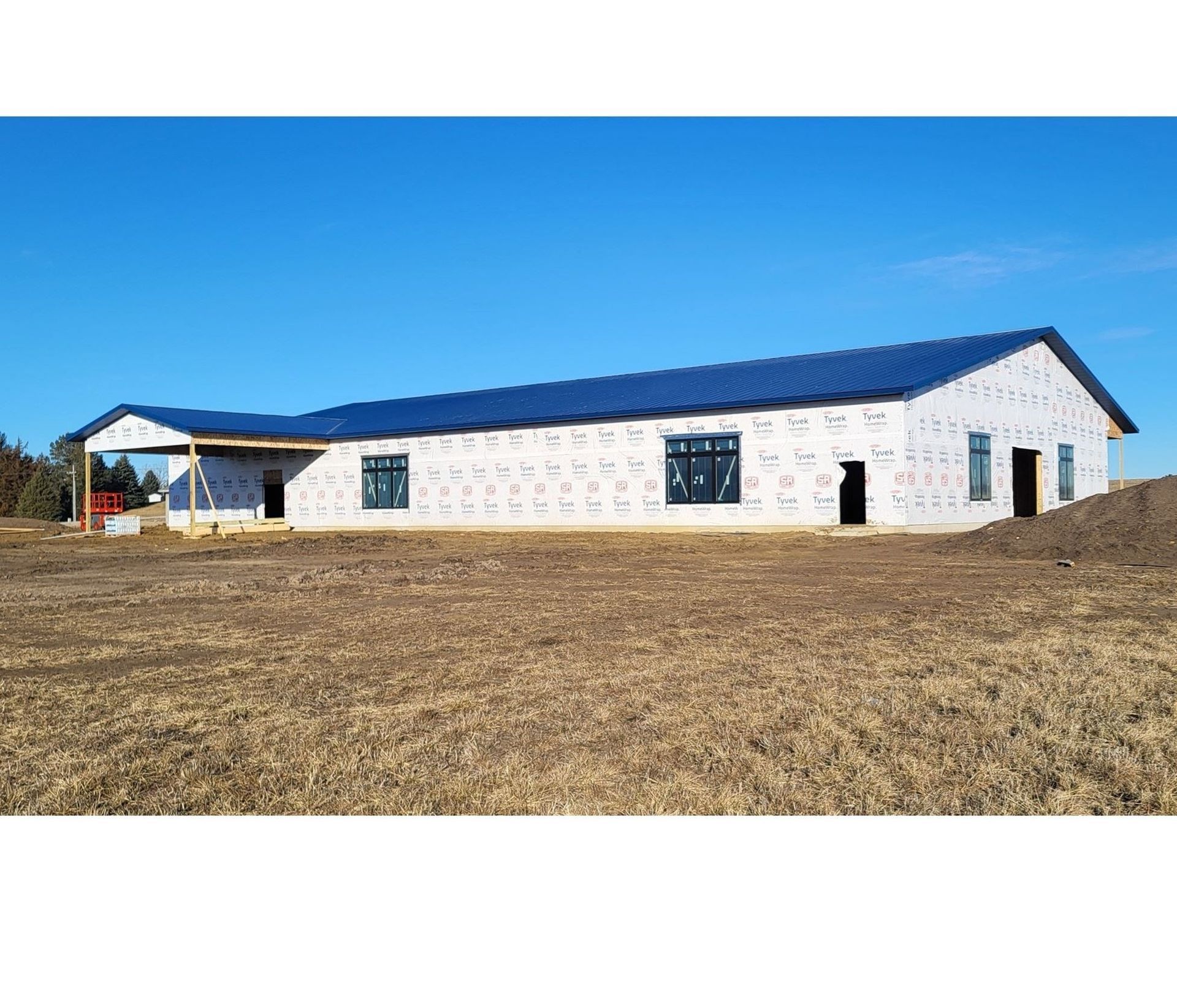 Long white single-story building with a blue roof on a bare field under a clear blue sky