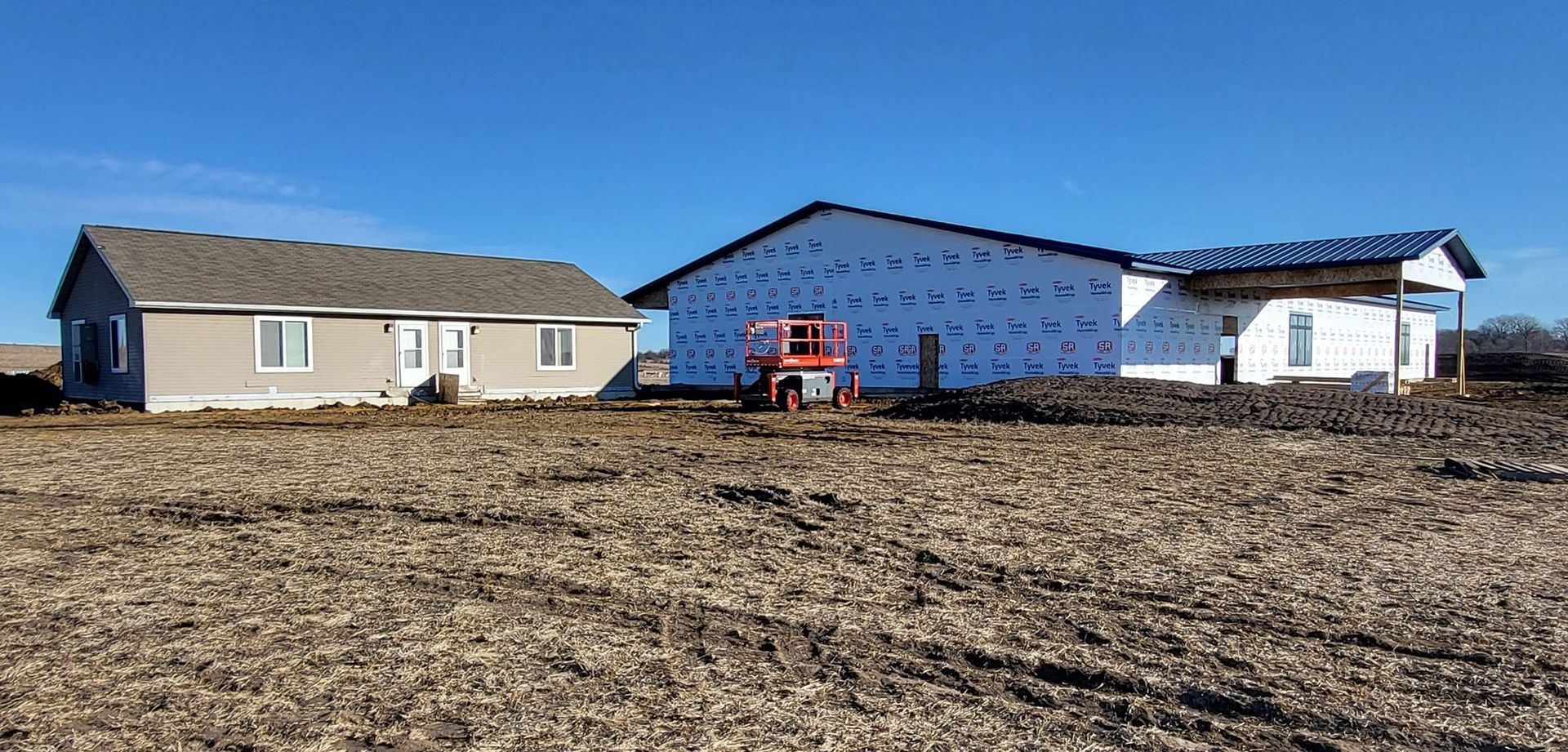 Three houses under construction in a dirt lot, with blue house wrap and a red utility lift.