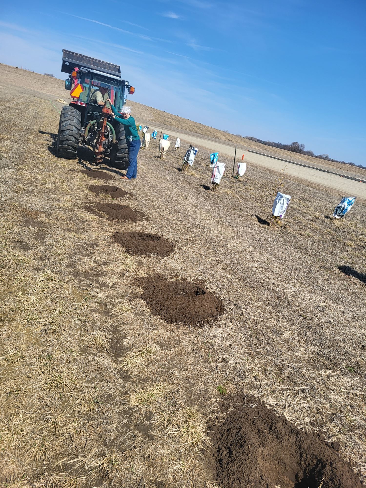 Farm workers planting in a dry field beside a tractor with rows of soil mounds