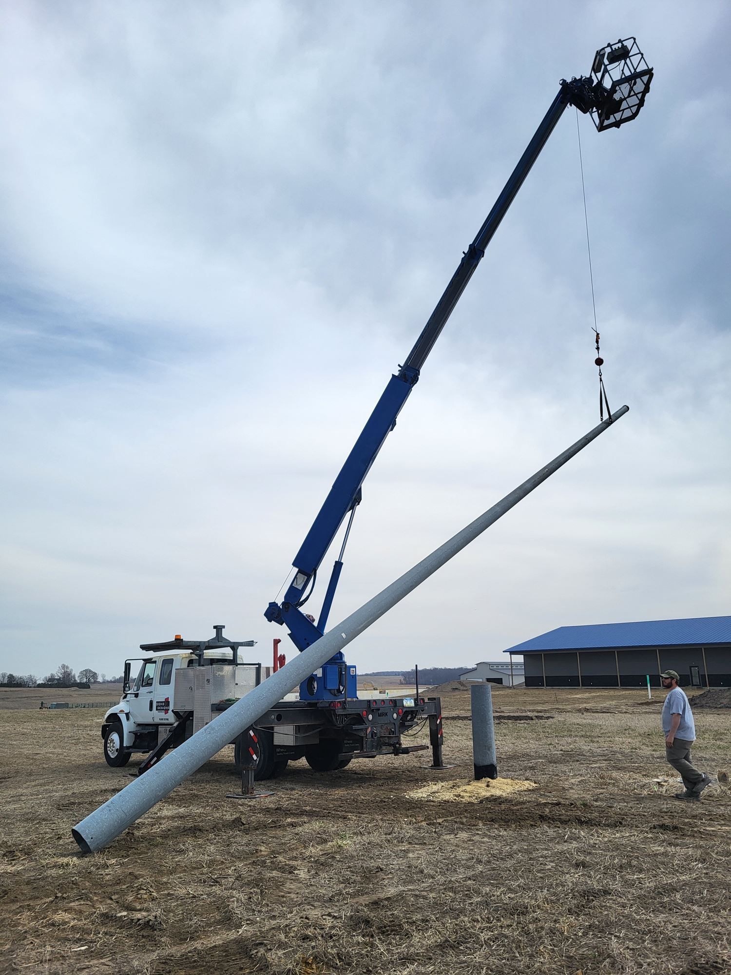 Crane hoisting a long utility pole onto a truck in an open field