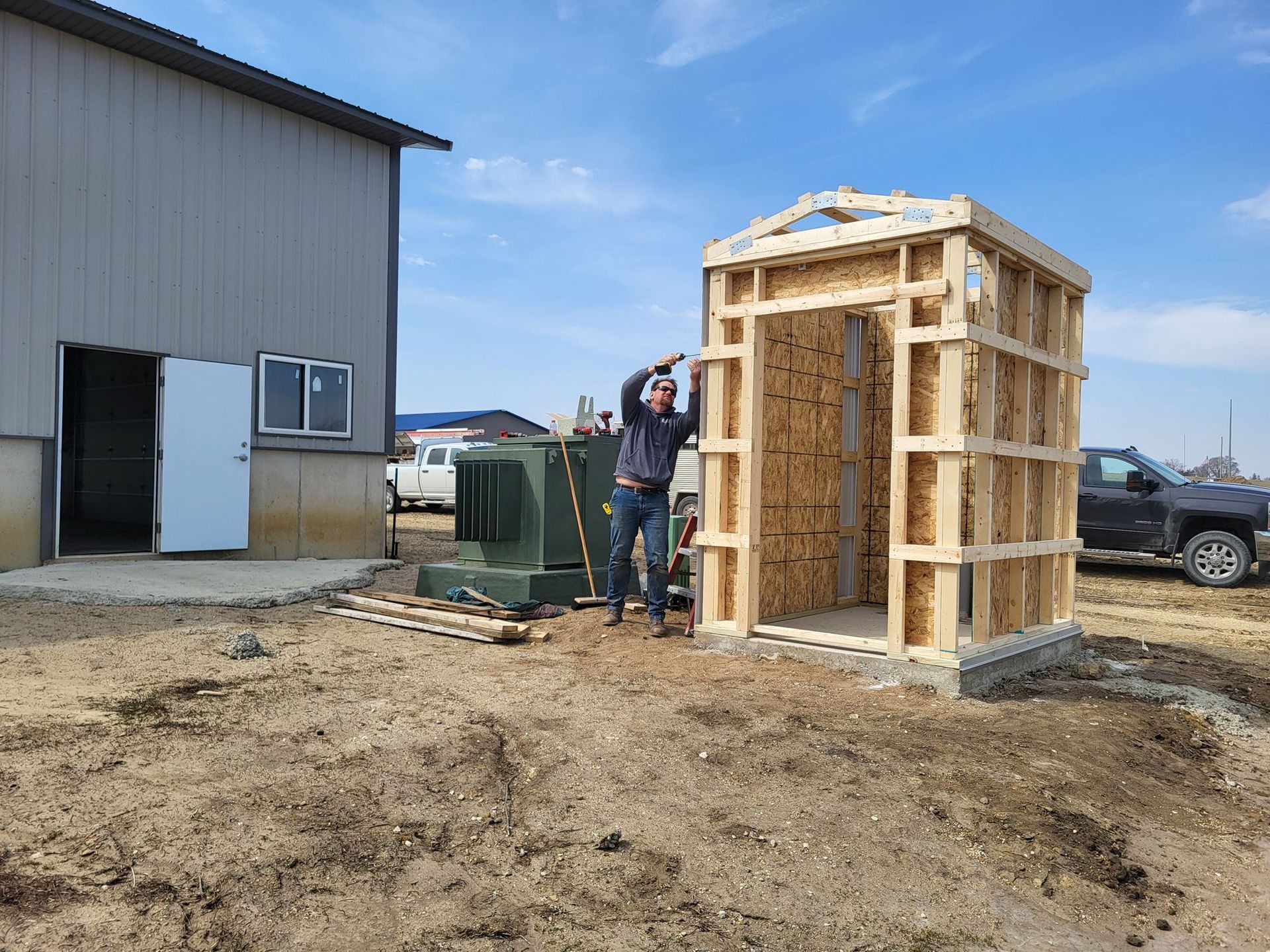 Person standing beside a small wooden structure at a construction site next to a building