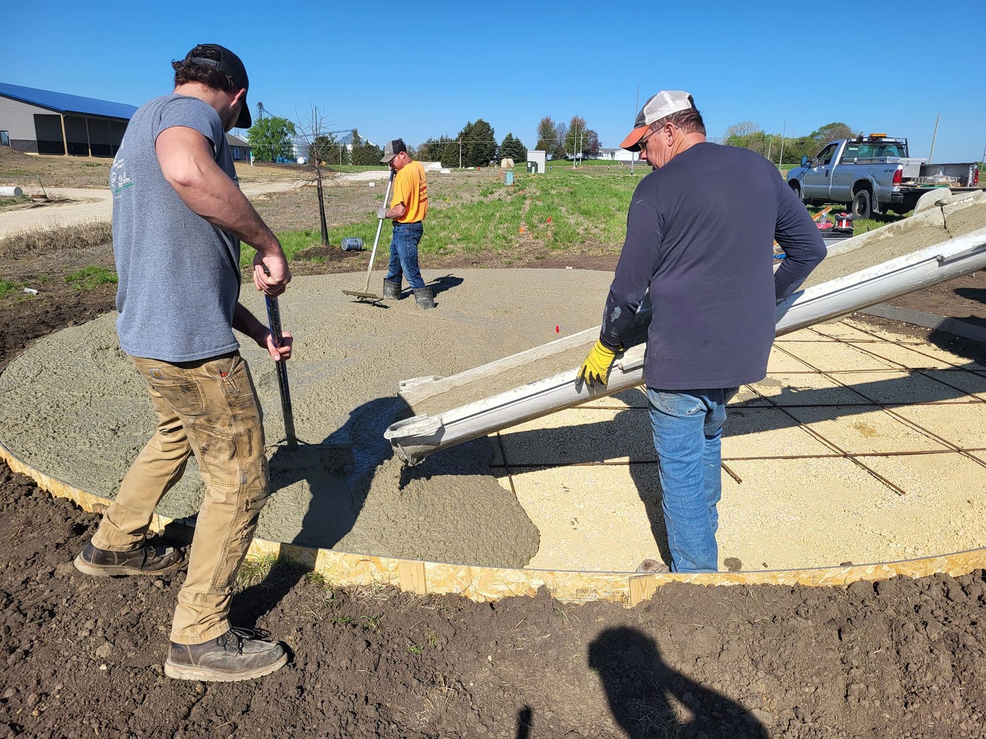 Workers moving a long white pipe across a dirt construction site on a sunny day