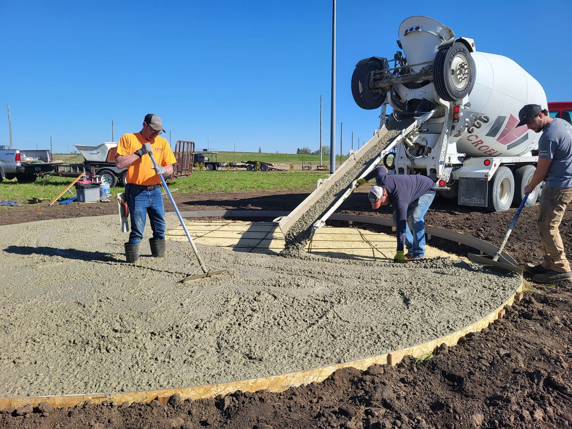 Concrete truck pouring a slab while workers rake and finish wet concrete outdoors