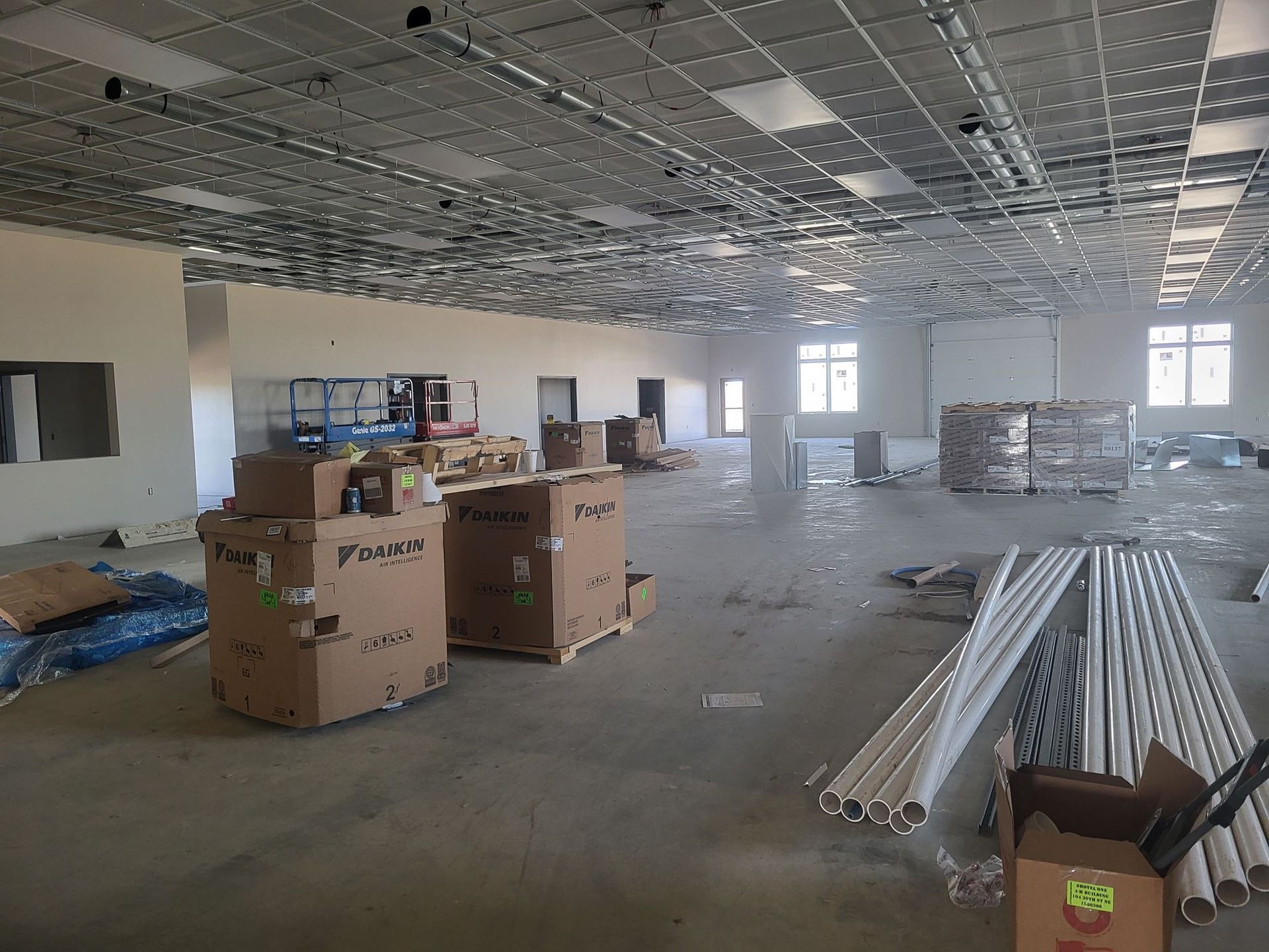 Empty unfinished office with boxes and metal beams on the floor under a grid ceiling.