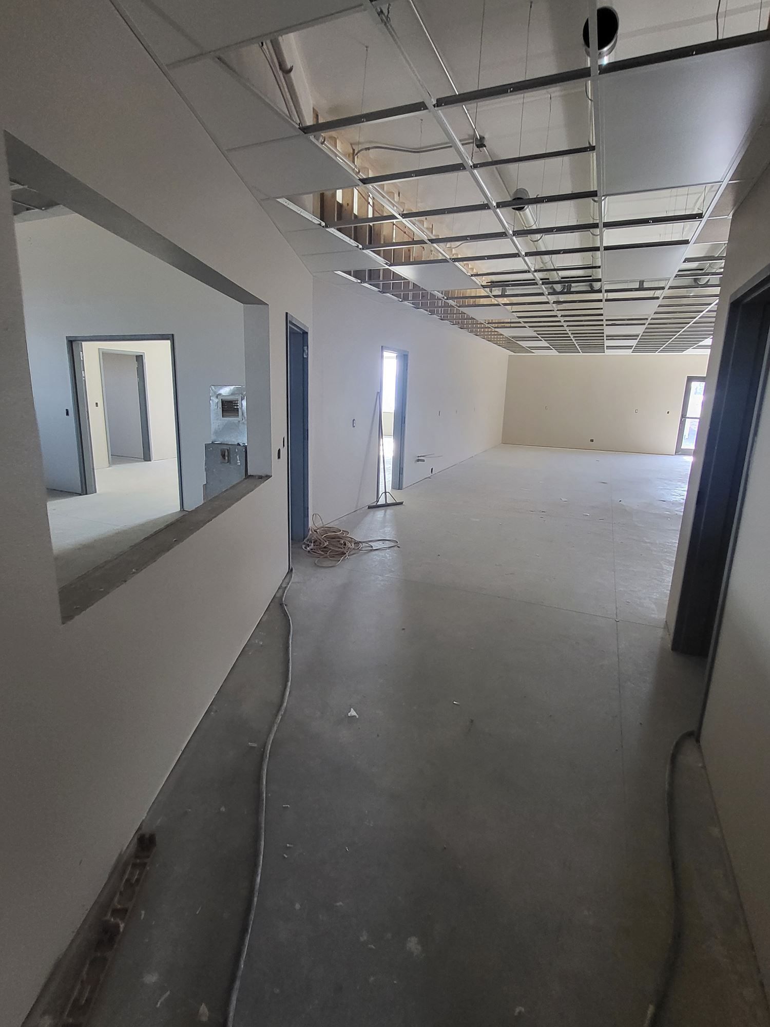 Empty unfinished interior hallway with exposed ceiling, gray floor, and white walls