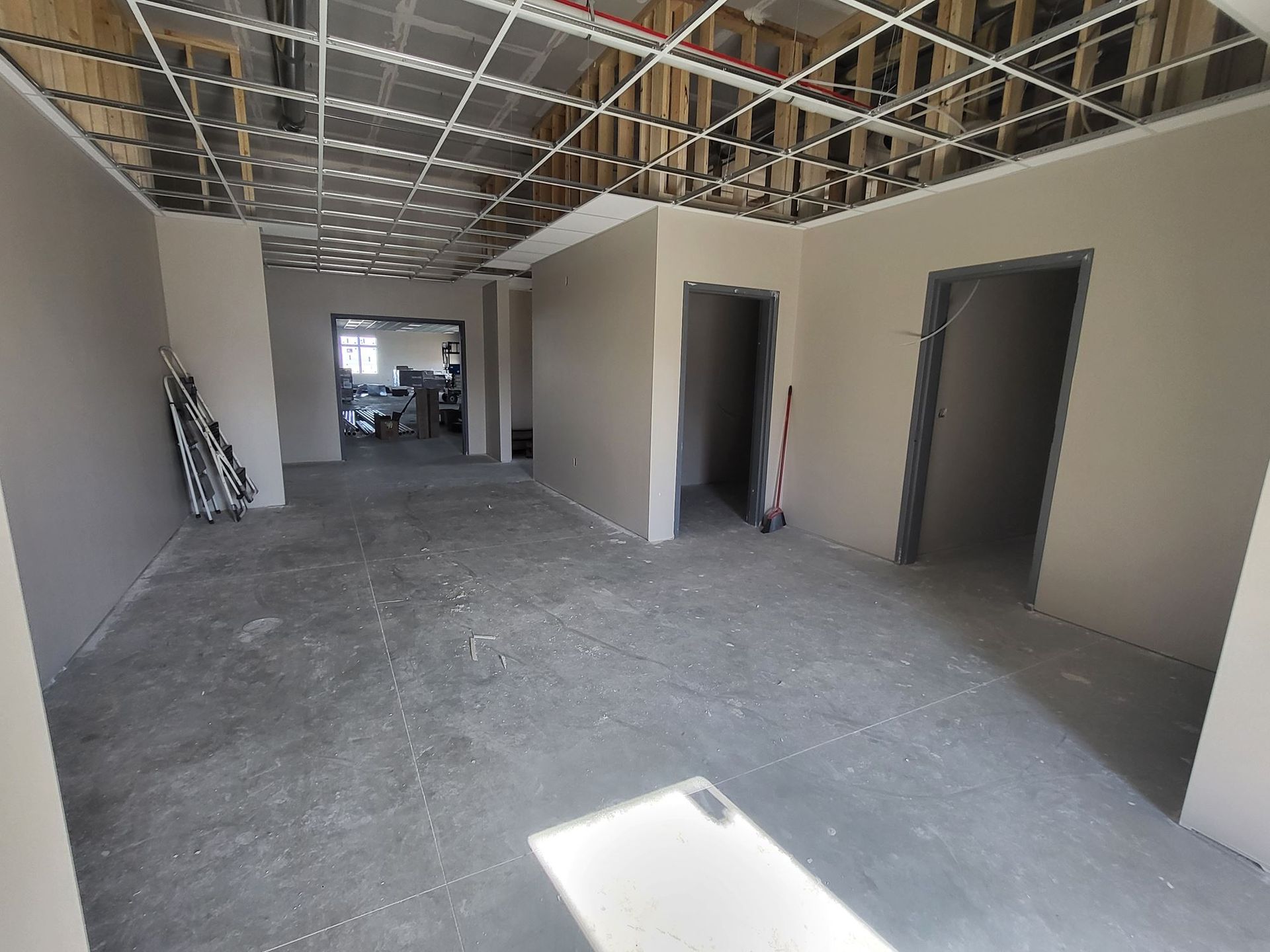 Empty unfinished hallway with open doorways, exposed ceiling, and concrete floor in a commercial building