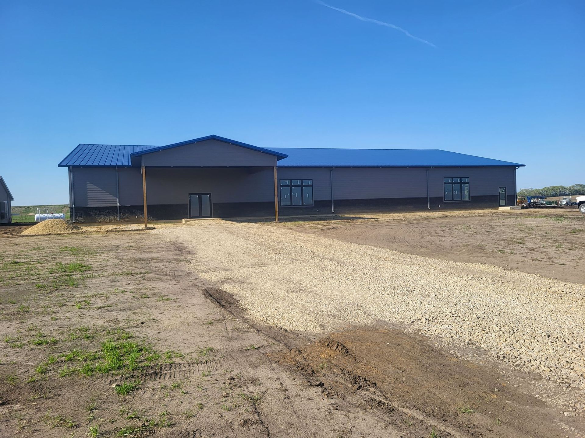 Large blue-roofed building on a dirt lot under a clear blue sky