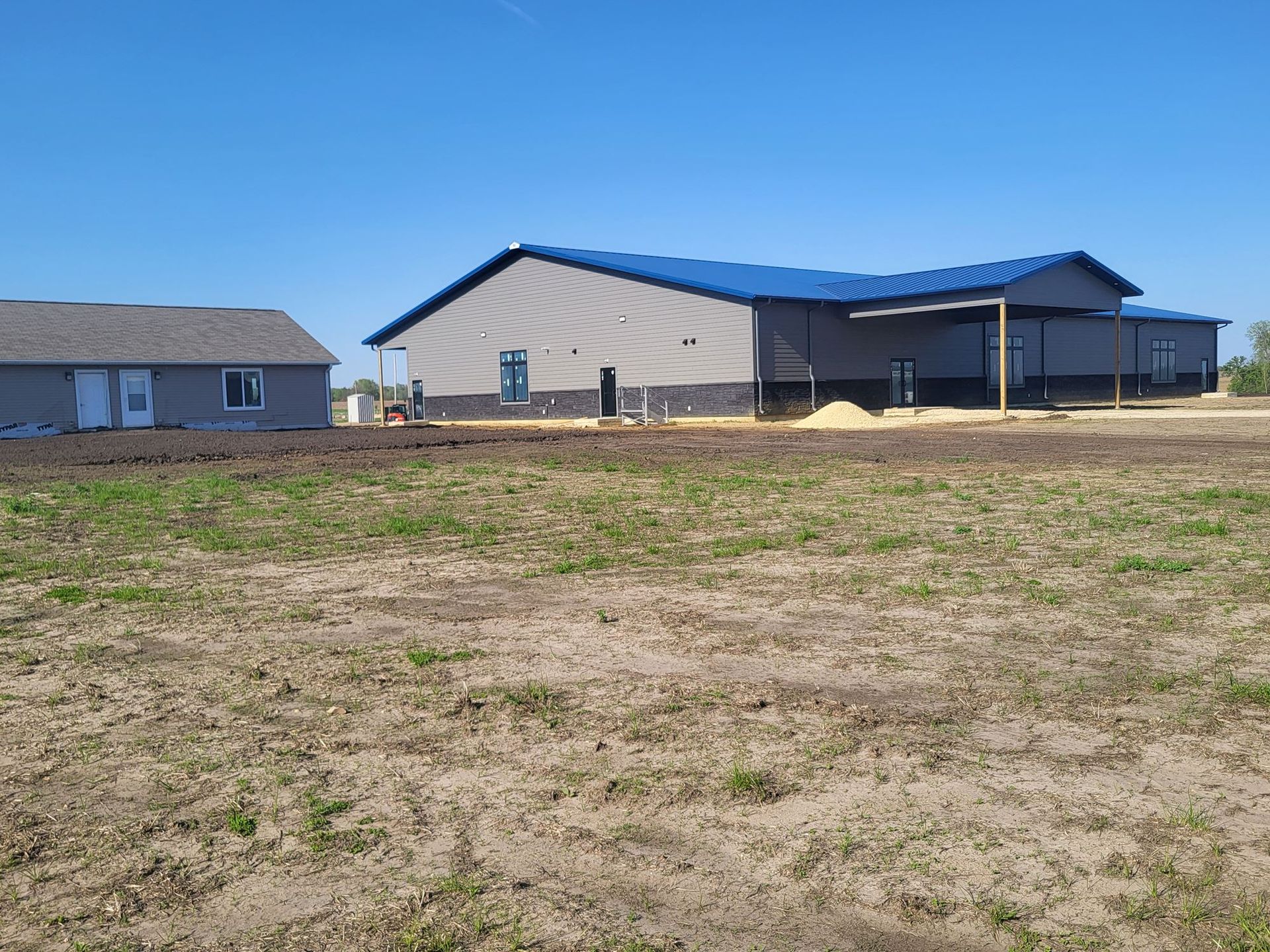 Two beige buildings with blue roofs in a dry grassy field under a clear blue sky.