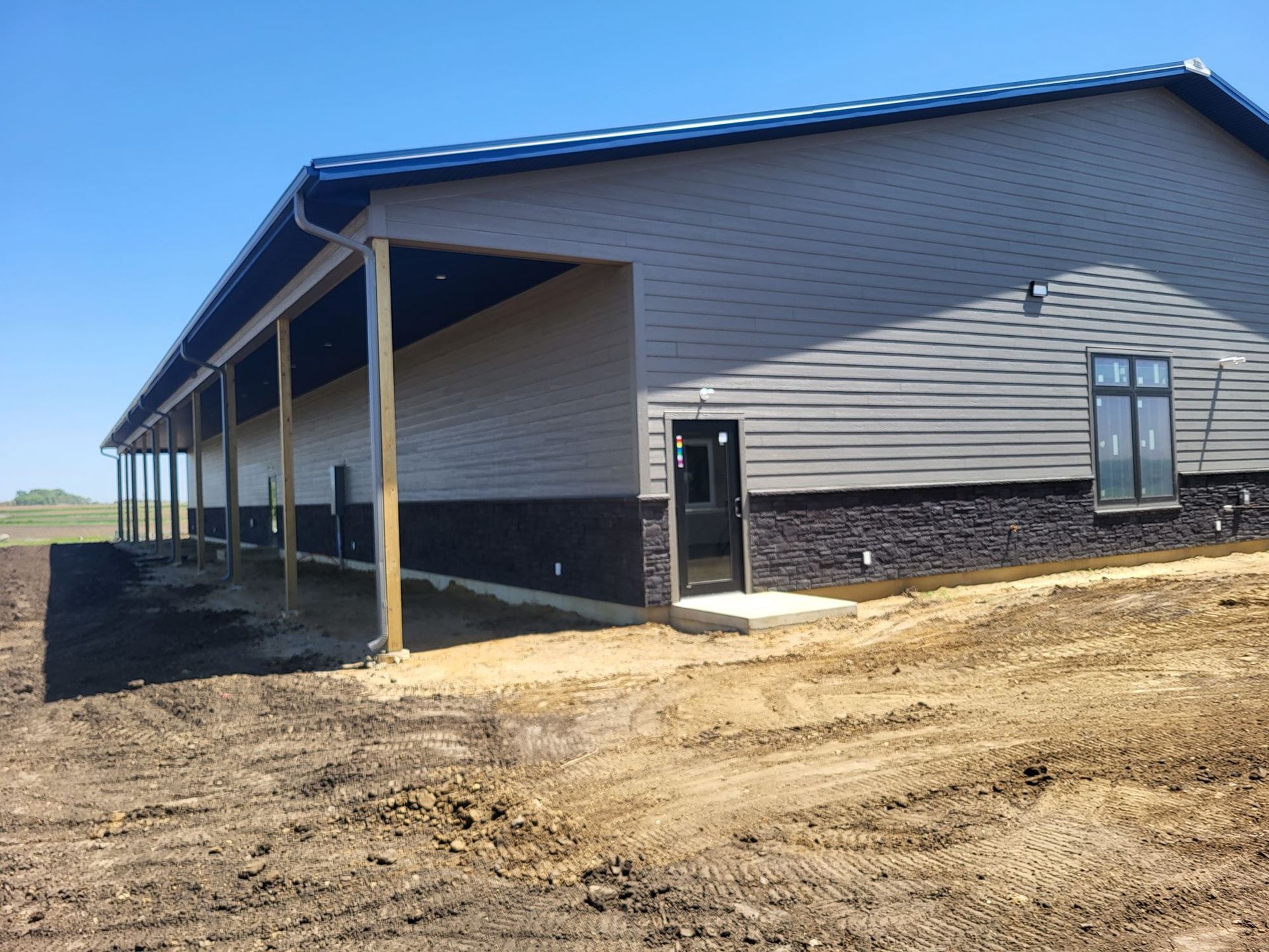 Partially built beige house with covered porch on a dirt lot under a blue sky