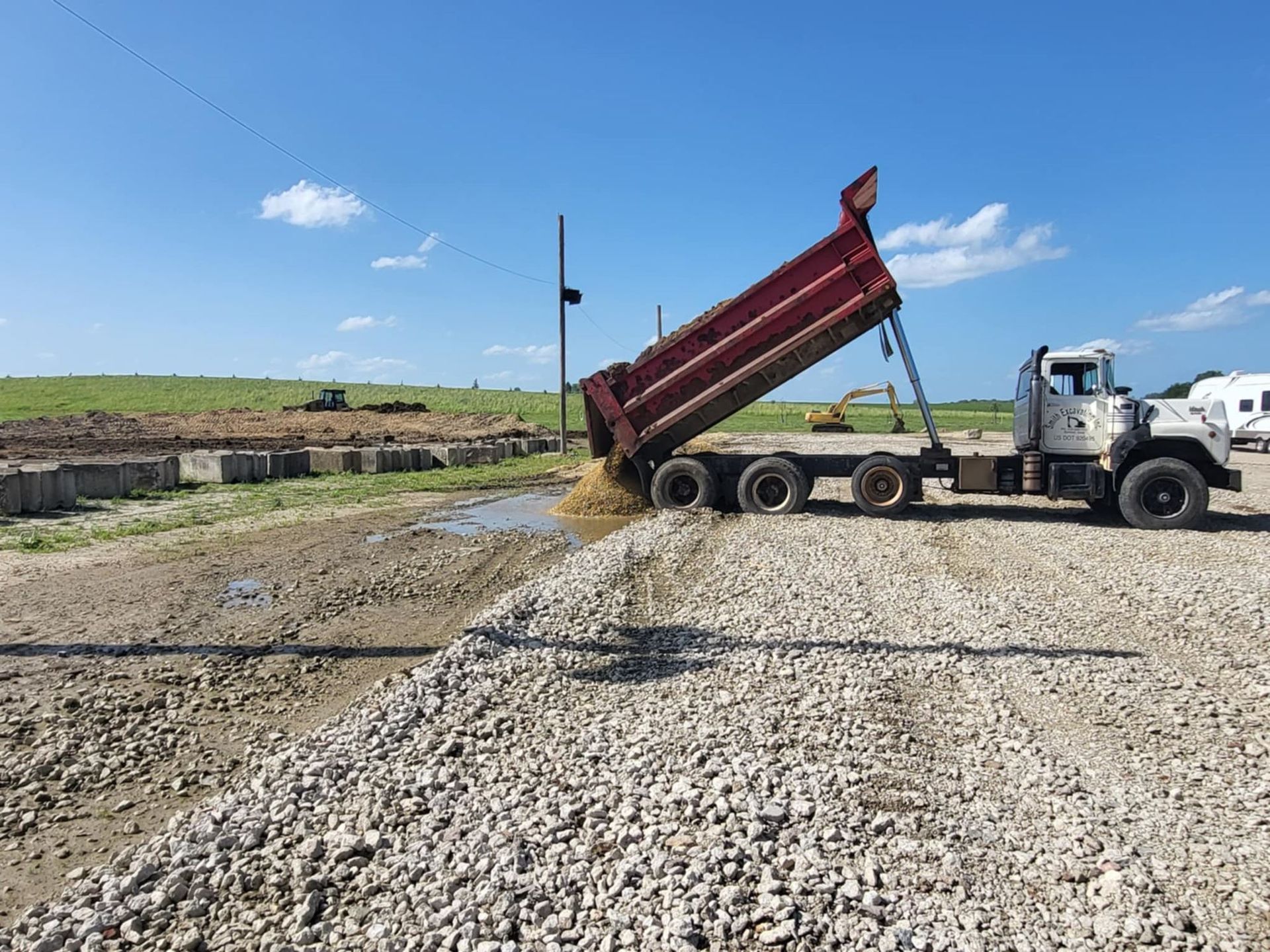 Dump truck unloading gravel at a construction site under a blue sky